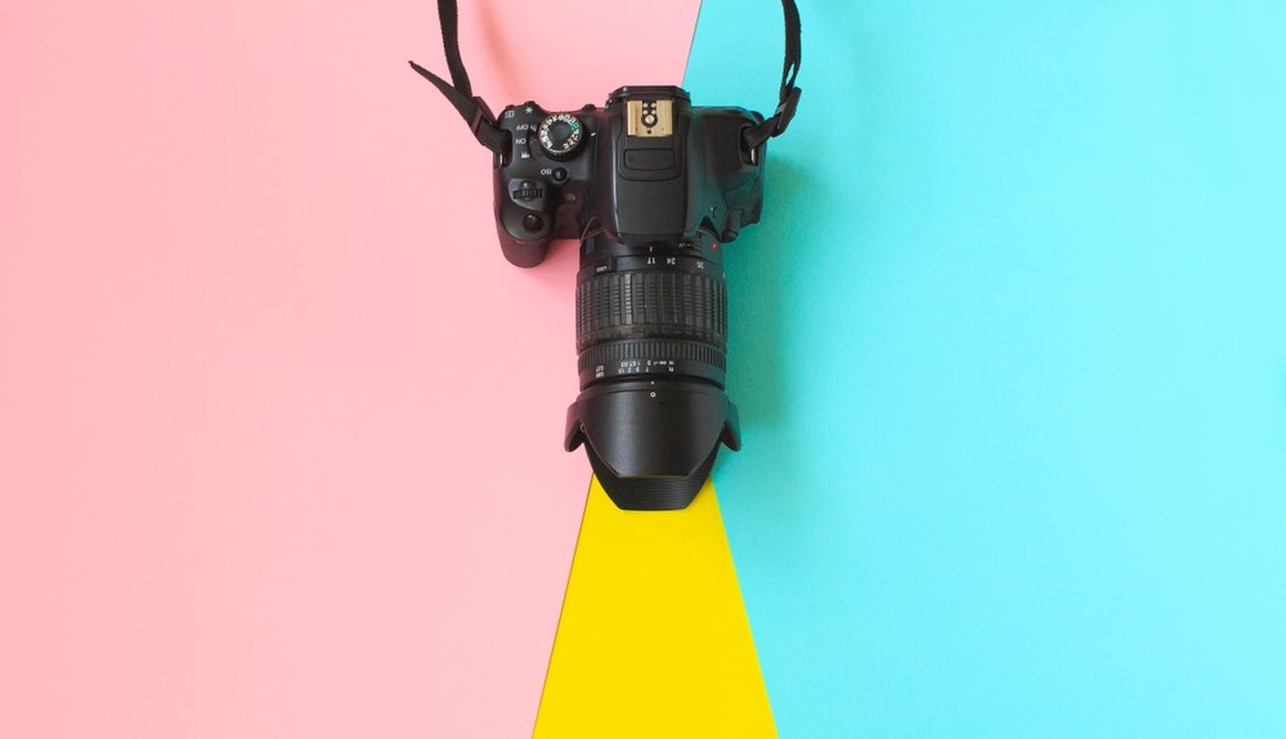 Plano cenital de una cámara réflex sobre un fondo rosa y azul. Del objetivo sale como un rayo de luz amarillo.