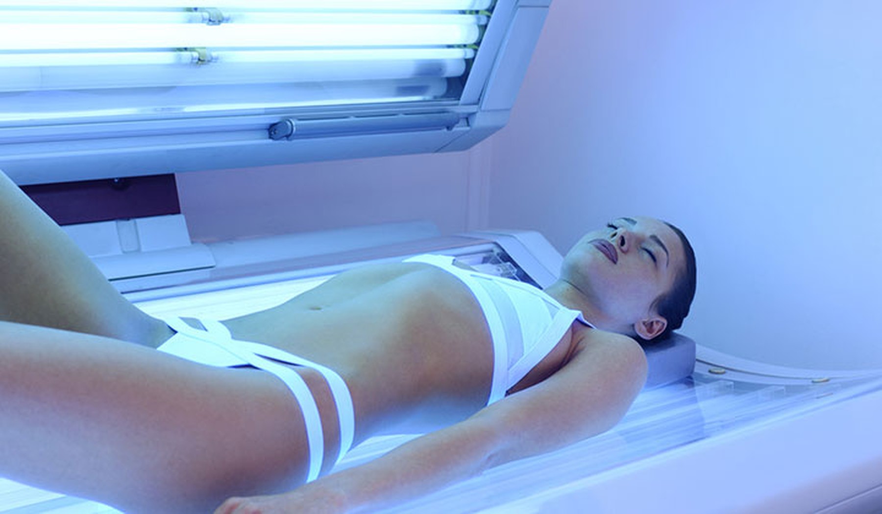 Mujer joven con un bikini blanco tumbada en una cama de rayos uva