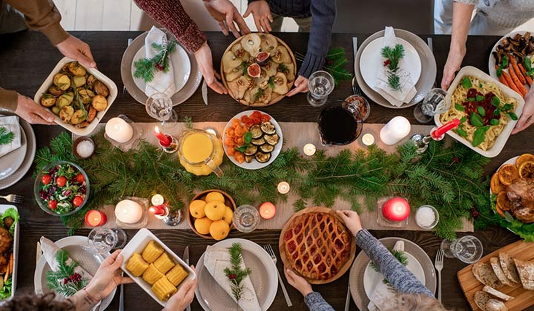 Plano cenital de una mesa decorada por Navidad con personas pasándose platos de comida