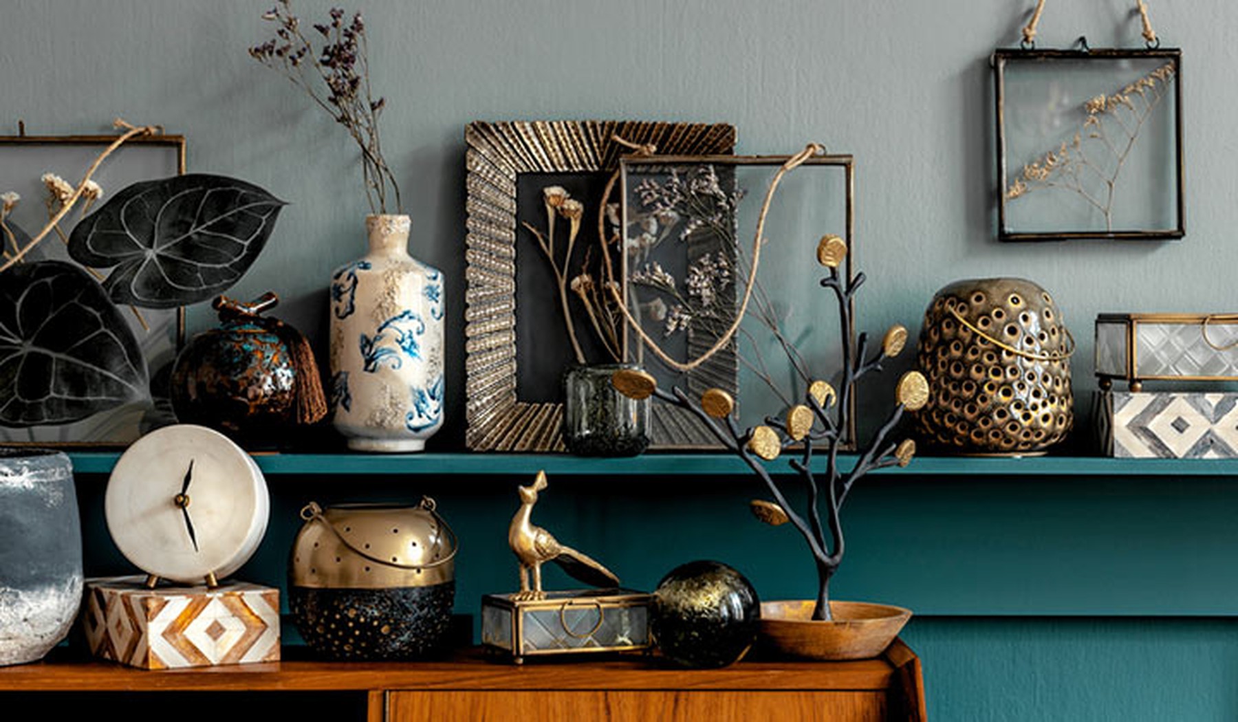 Accesorios de decoración vintage en una balda de madera azul verdosa y un mueble de madera. Hay marcos de fotos, jarrones, esculturas de plantas...