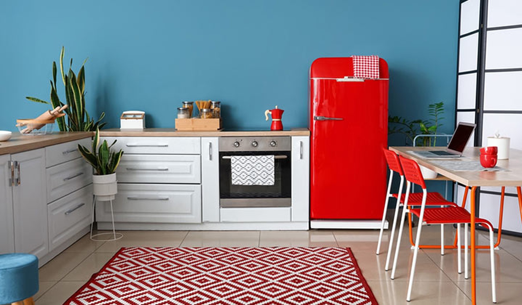 Cocina con muebles blancos y de madera, una alfombra geométrica blanca y roja y un frigorífico rojo estilo retro