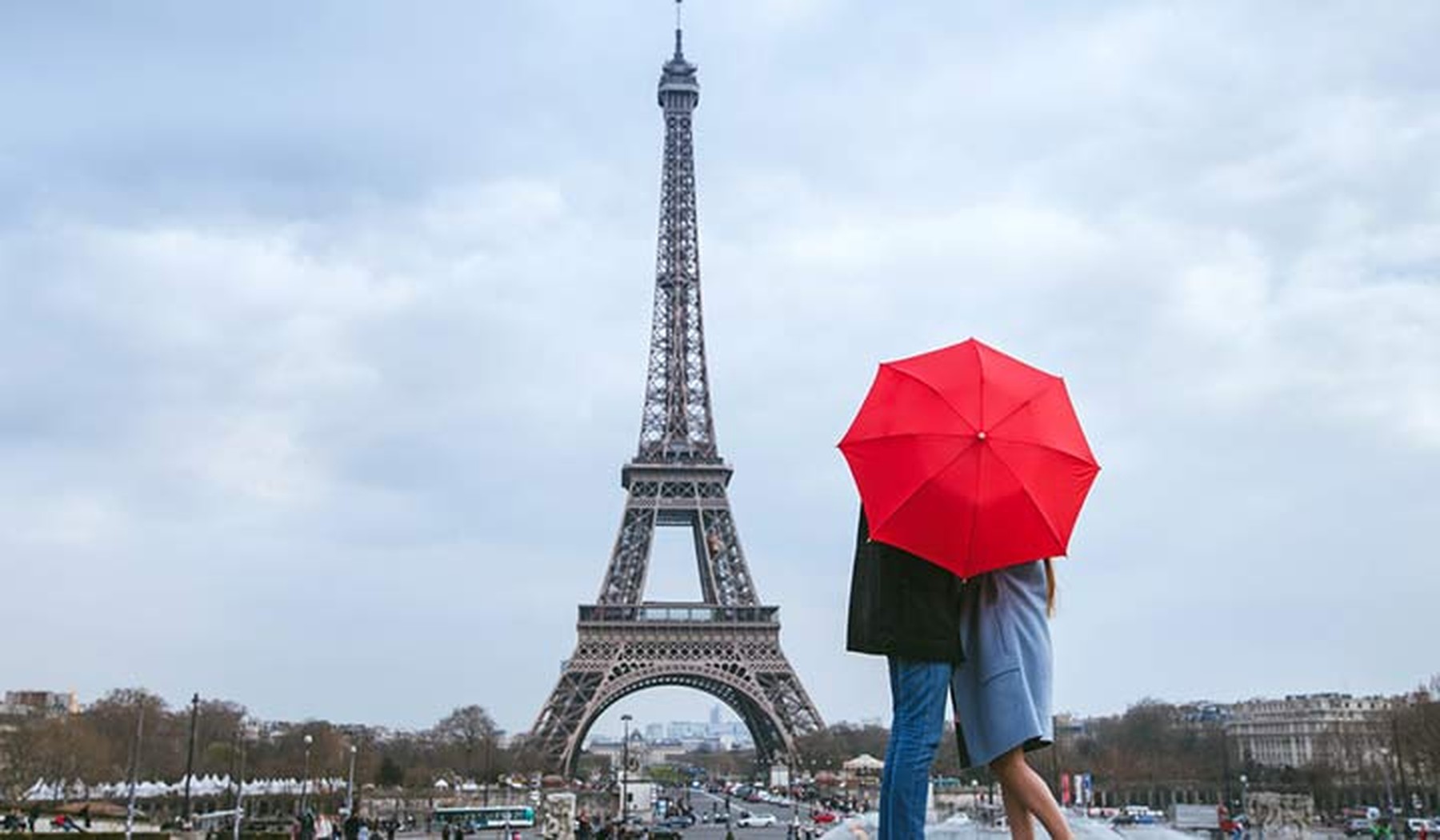 Pareja escondidos tras un paraguas rojo observando la Torre Eiffel en un día nublado