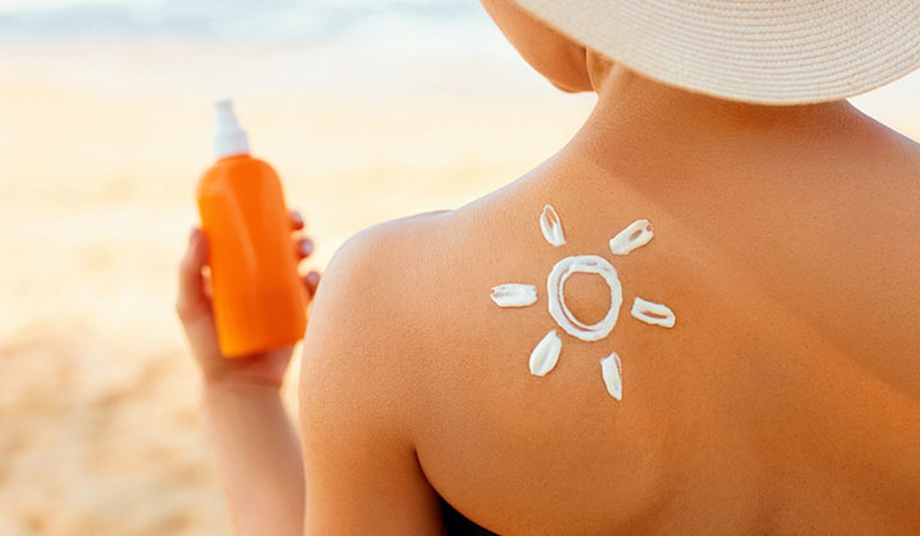 Espalda de mujer con un tono de bronceado y un sol dibujado con crema solar. En la mano sostiene un bote de crema naranja.