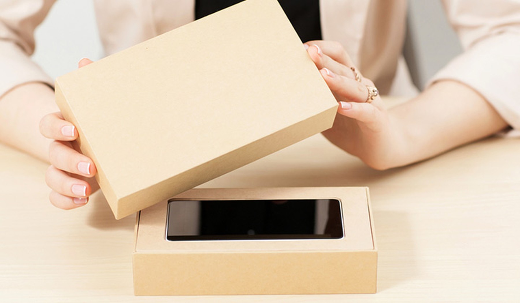 Mujer destapando una caja beige con un smartphone nuevo dentro