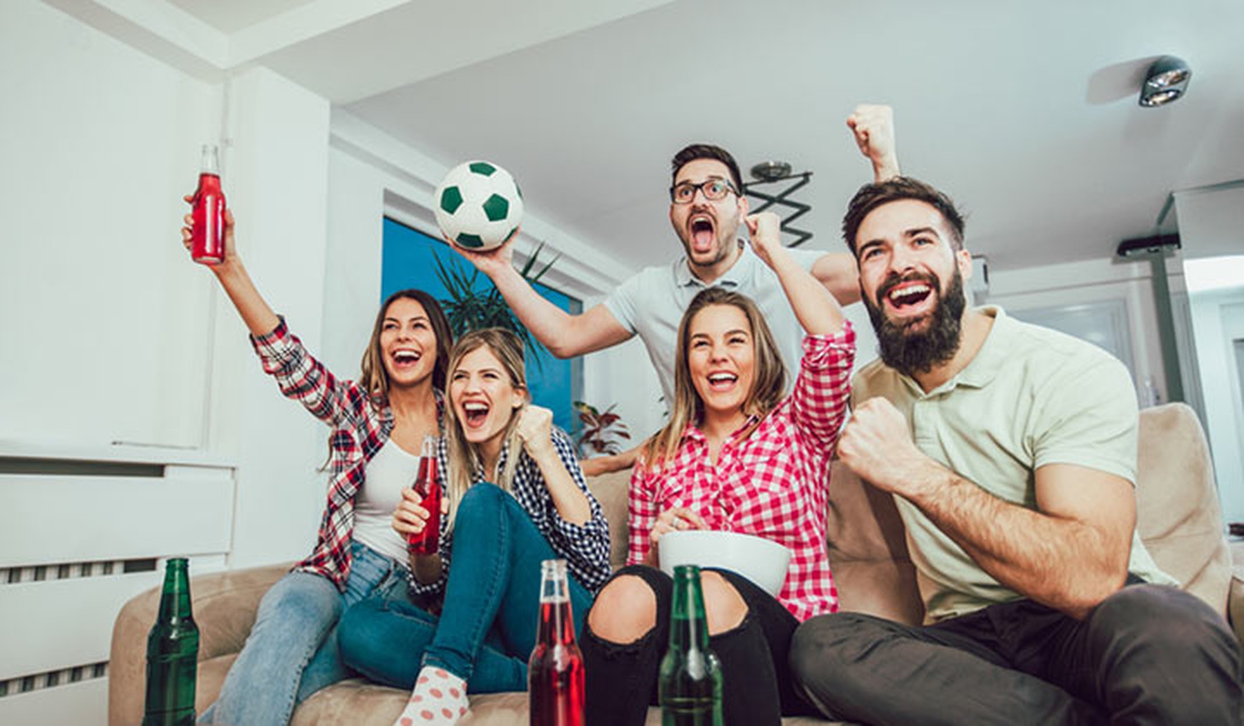 Grupo de amigos con cervezas celebrando un gol en el sofá de casa