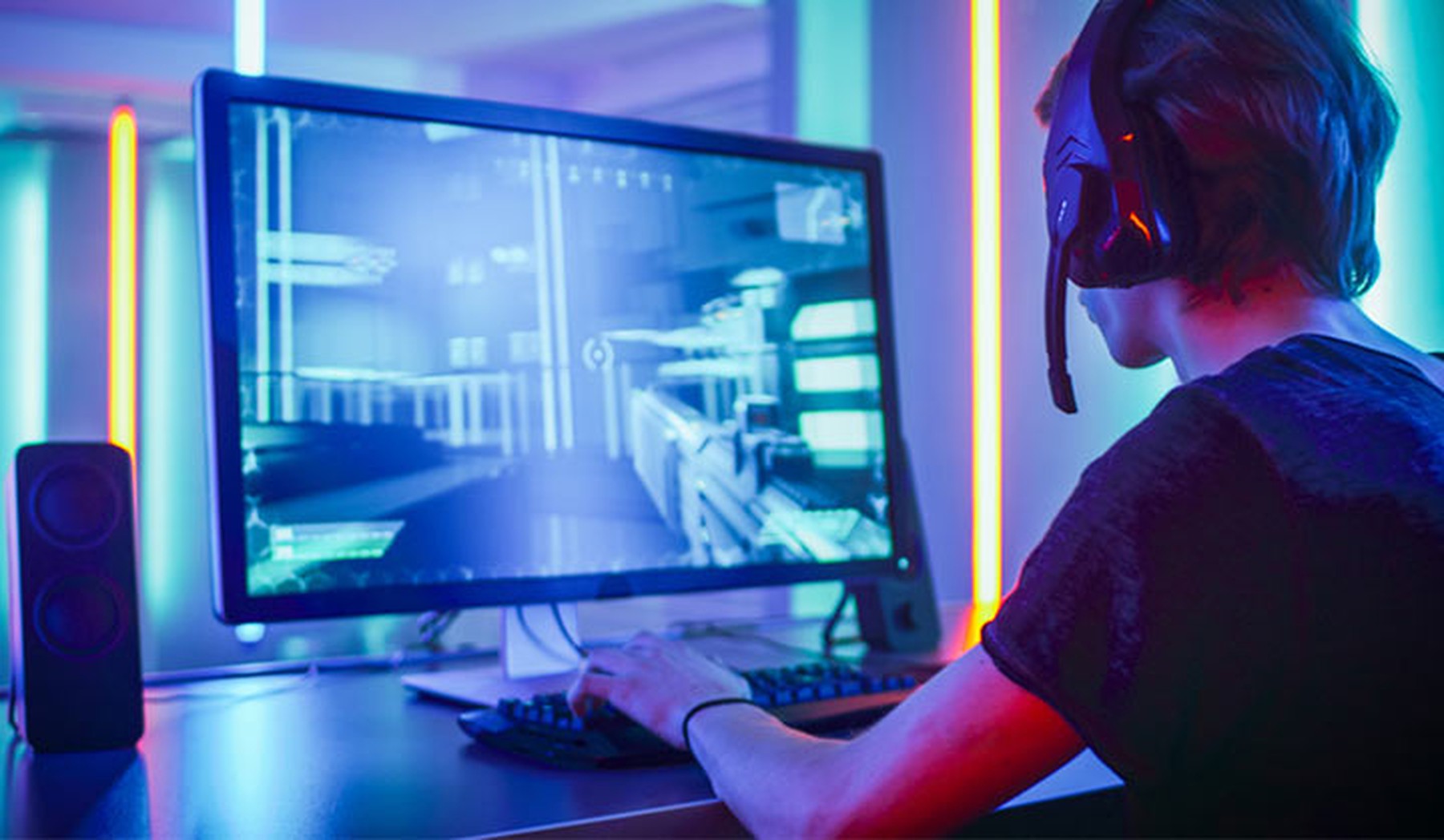 Chico joven con cascos inalámbricos de gamer con micrófono jugando a un vídeojuego en el ordenador