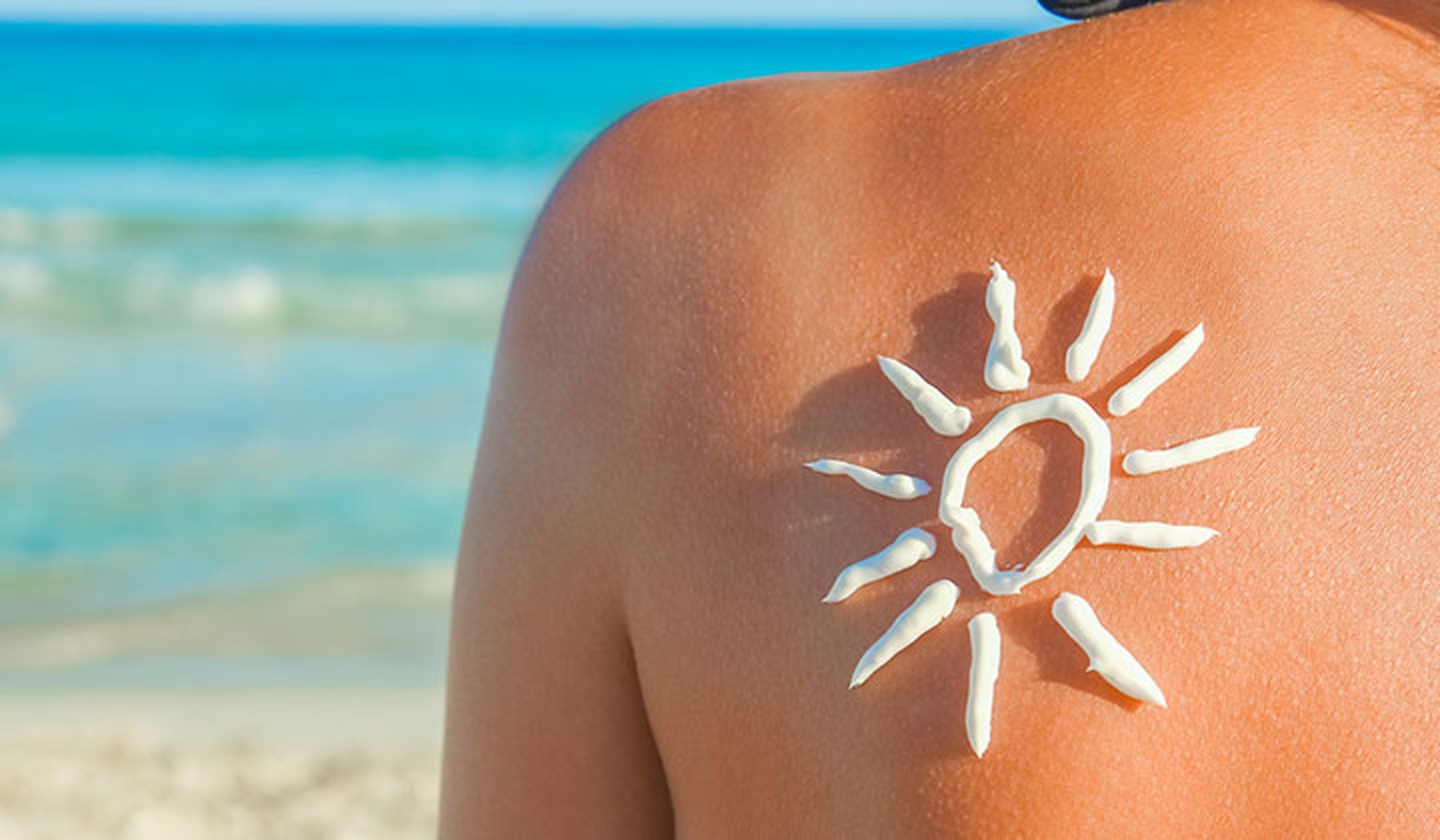 Espalda de una mujer con marcas de moreno y un sol dibujado con crema solar. De fondo se ve el mar.