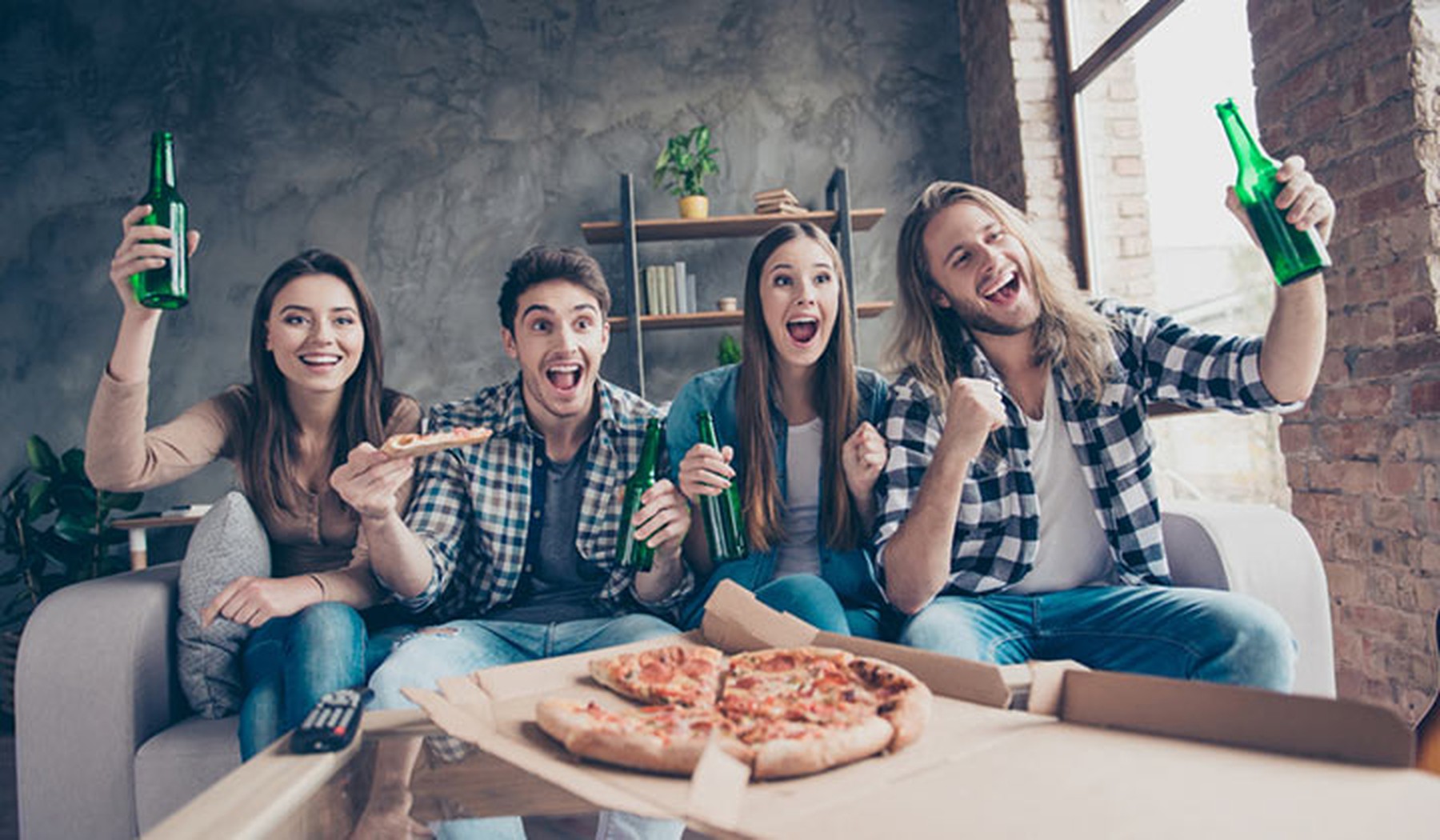 Grupo de amigos viendo un partido de fútbol con pizzas y cervezas