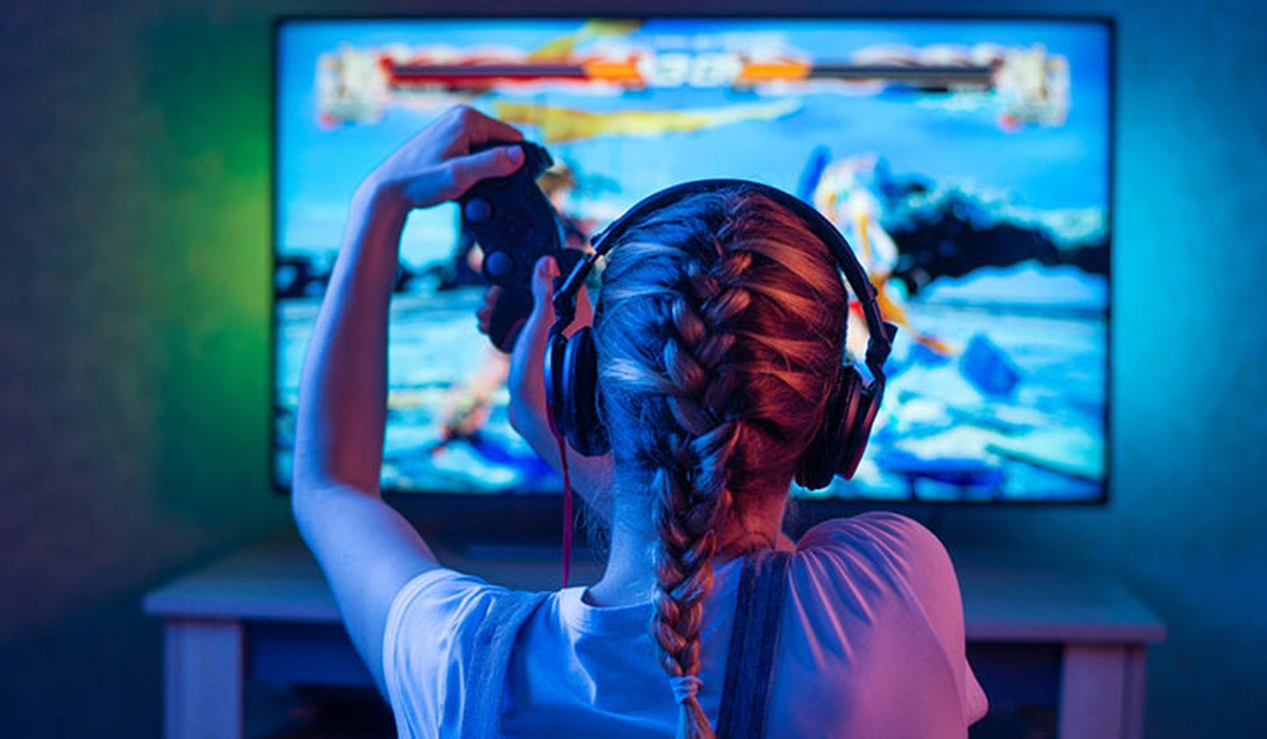 chica rubia con una trenza y cascos de gamer jugando a un videojuego en la televisión