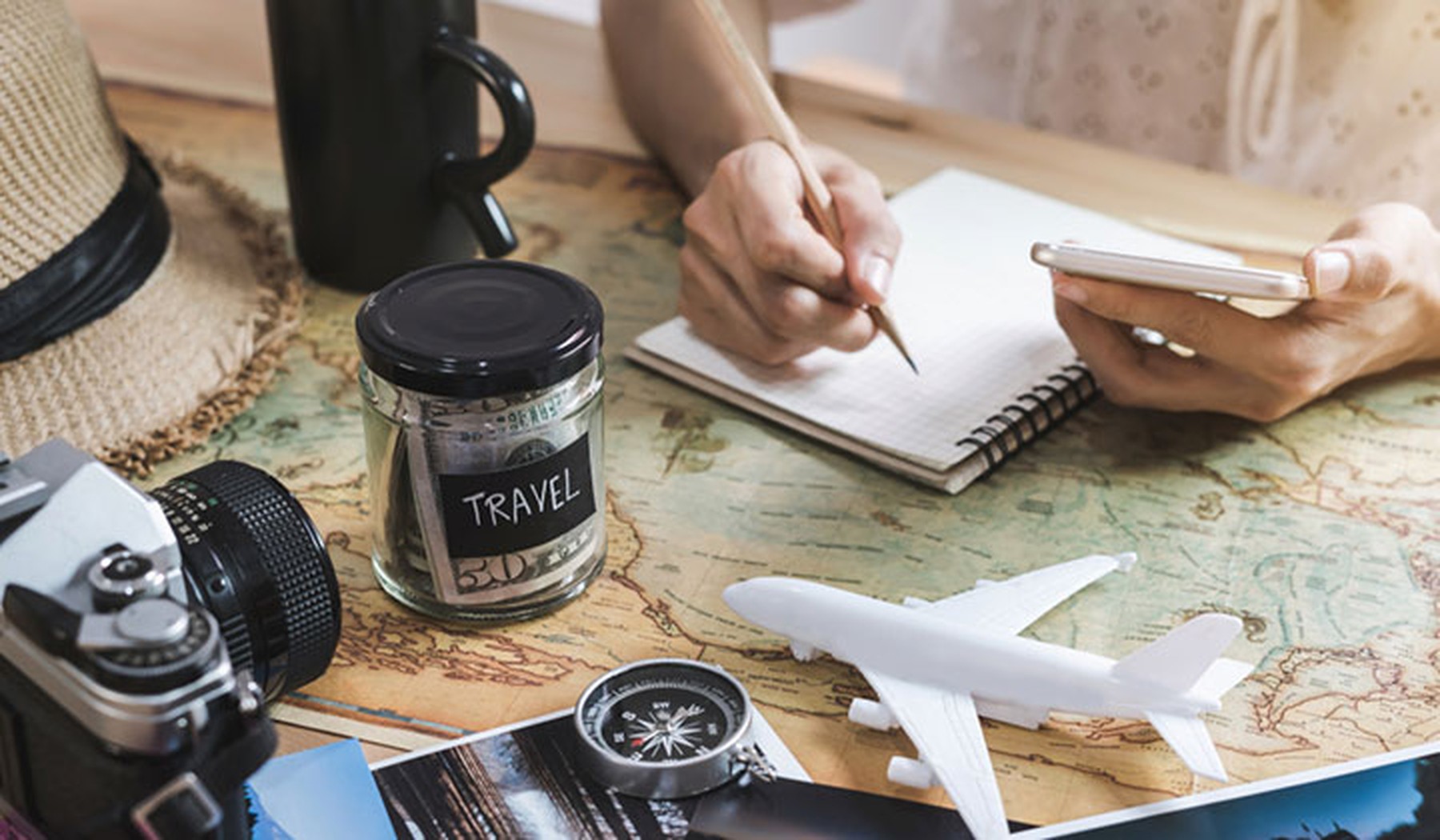 Persona escribiendo en un cuaderno y planeando un viaje sobre un mapa con una maqueta de un avión y sus ahorros