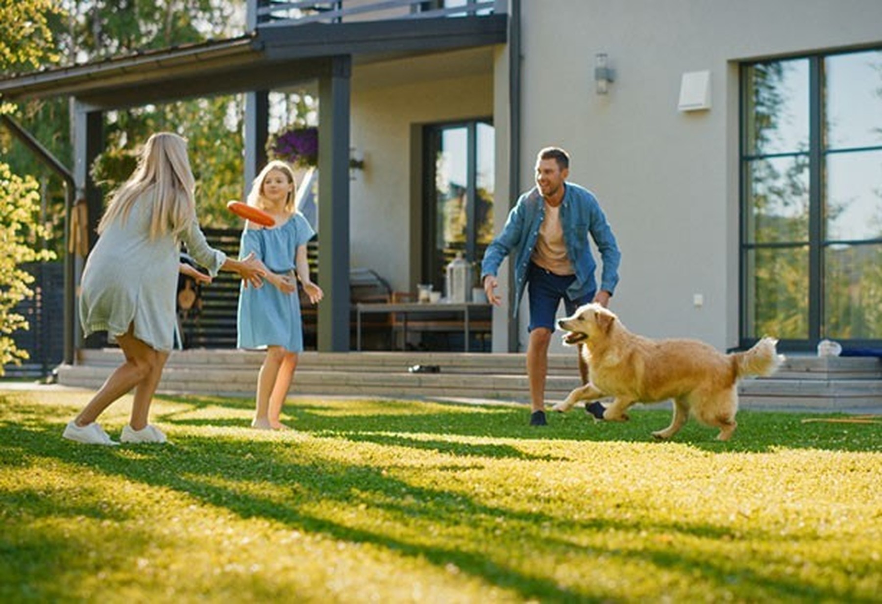 Familia de una madre, un padre y una hija jugando al frisbee en su jardín con su perro