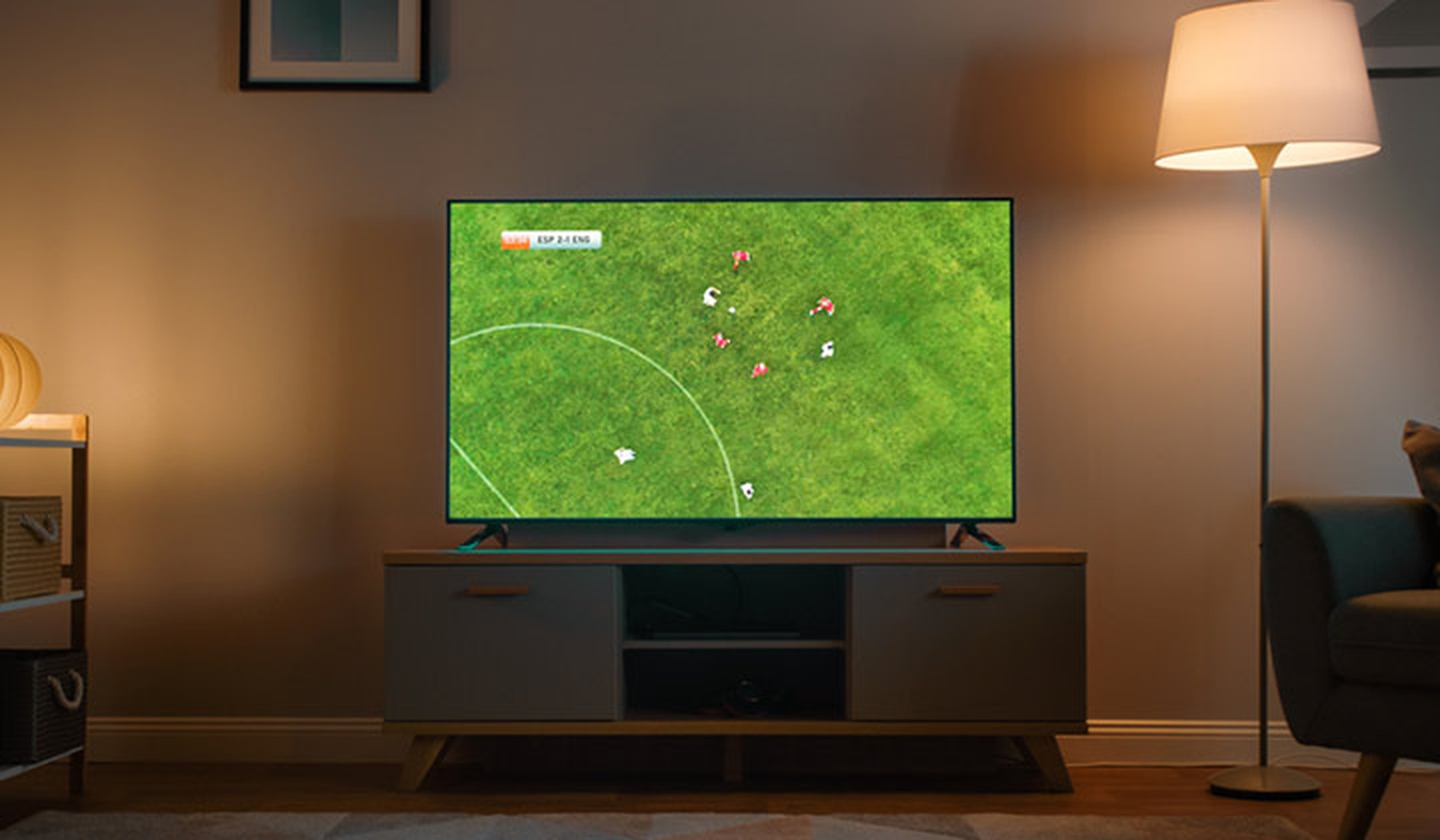 Televisión plana con un partido de fútbol en un salón con luz tenue