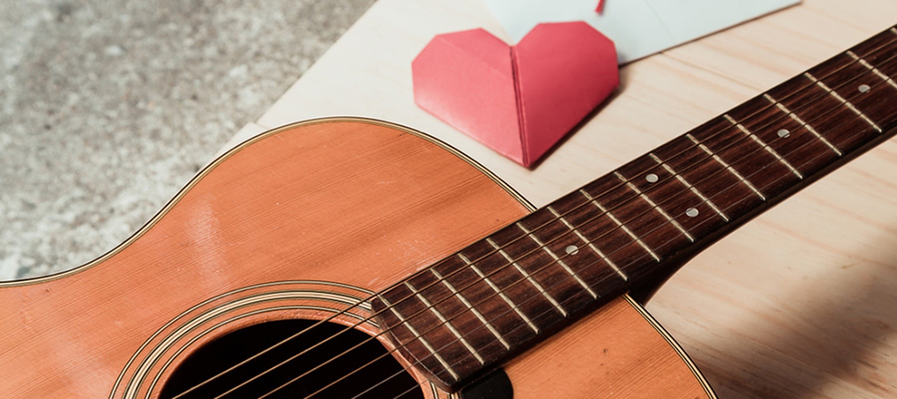 Guitarra sobre una mesa donde se encuentra también un corazón de papiroflexia en color rojo