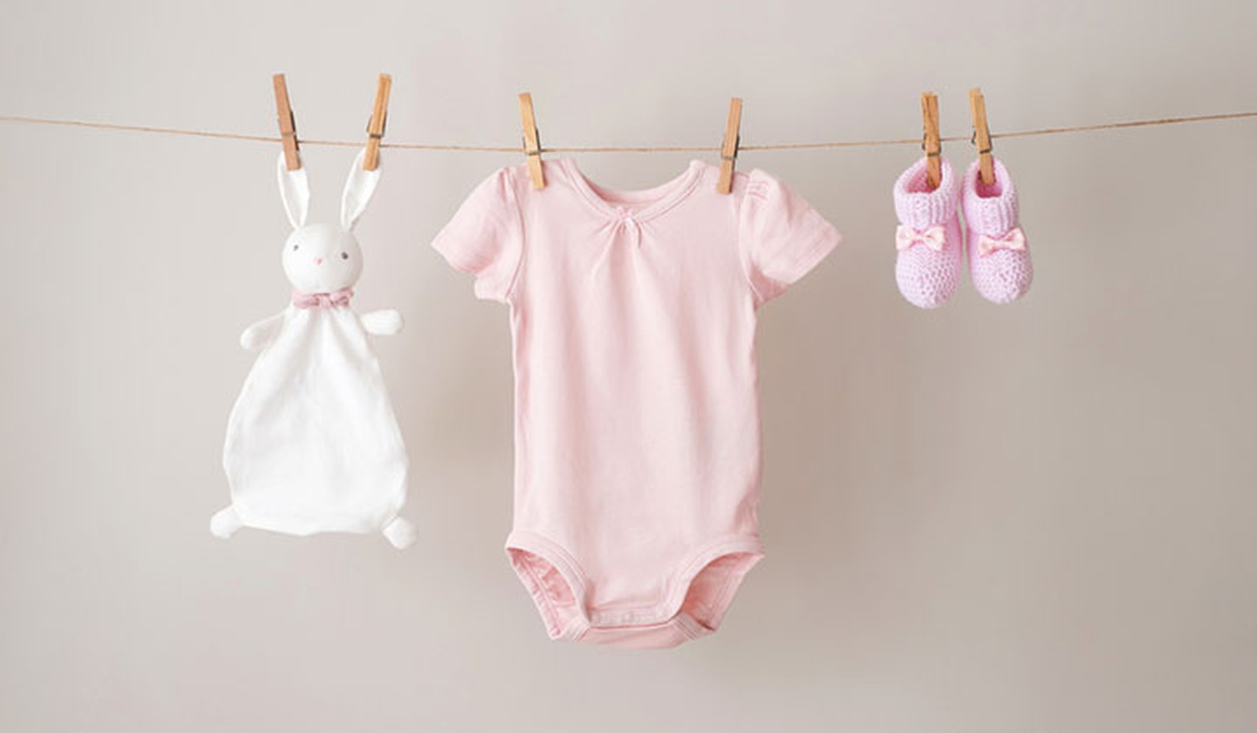 Bodie rosa de bebé, zapatos y peluche tendidos en una cuerda con pinzas