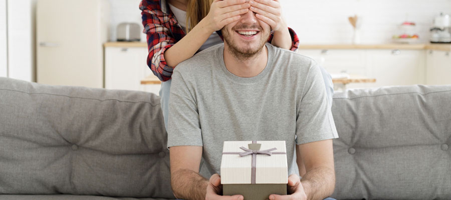Chica tapando los ojos a un chico con un regalo en sus manos