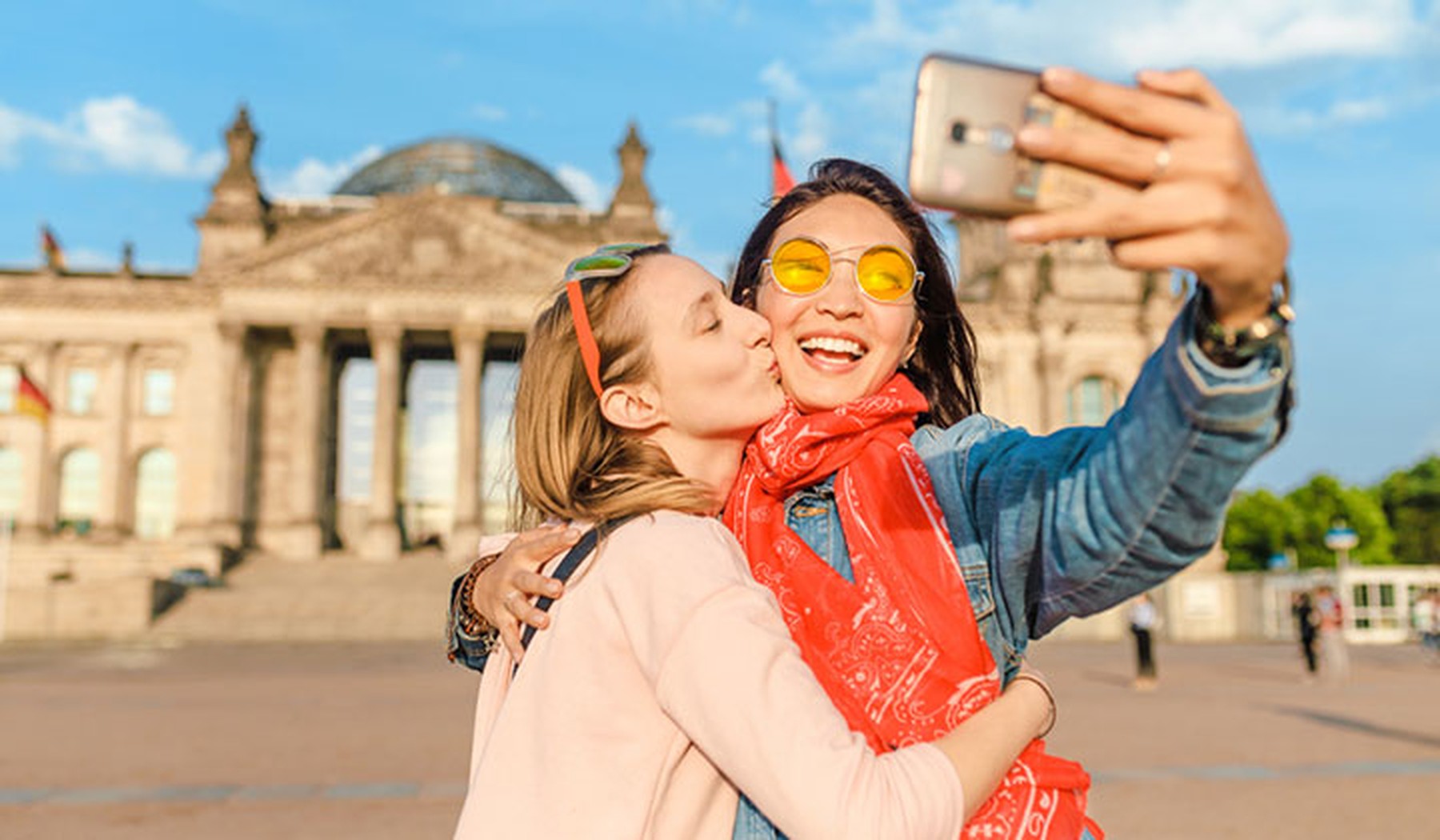 Pareja de dos mujeres jóvenes haciéndose un selfie frente a un monumento