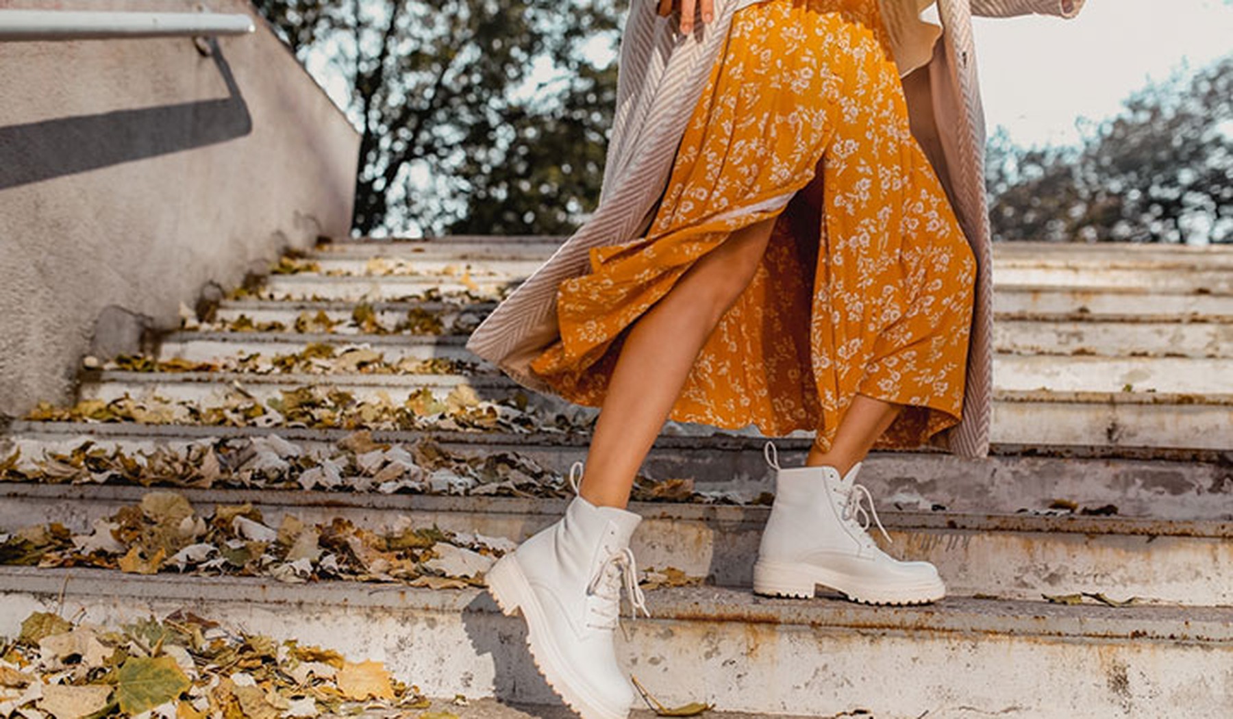 Parte de abajo de una mujer subiendo unas escaleras con una falda de flores naranja y botines blancos