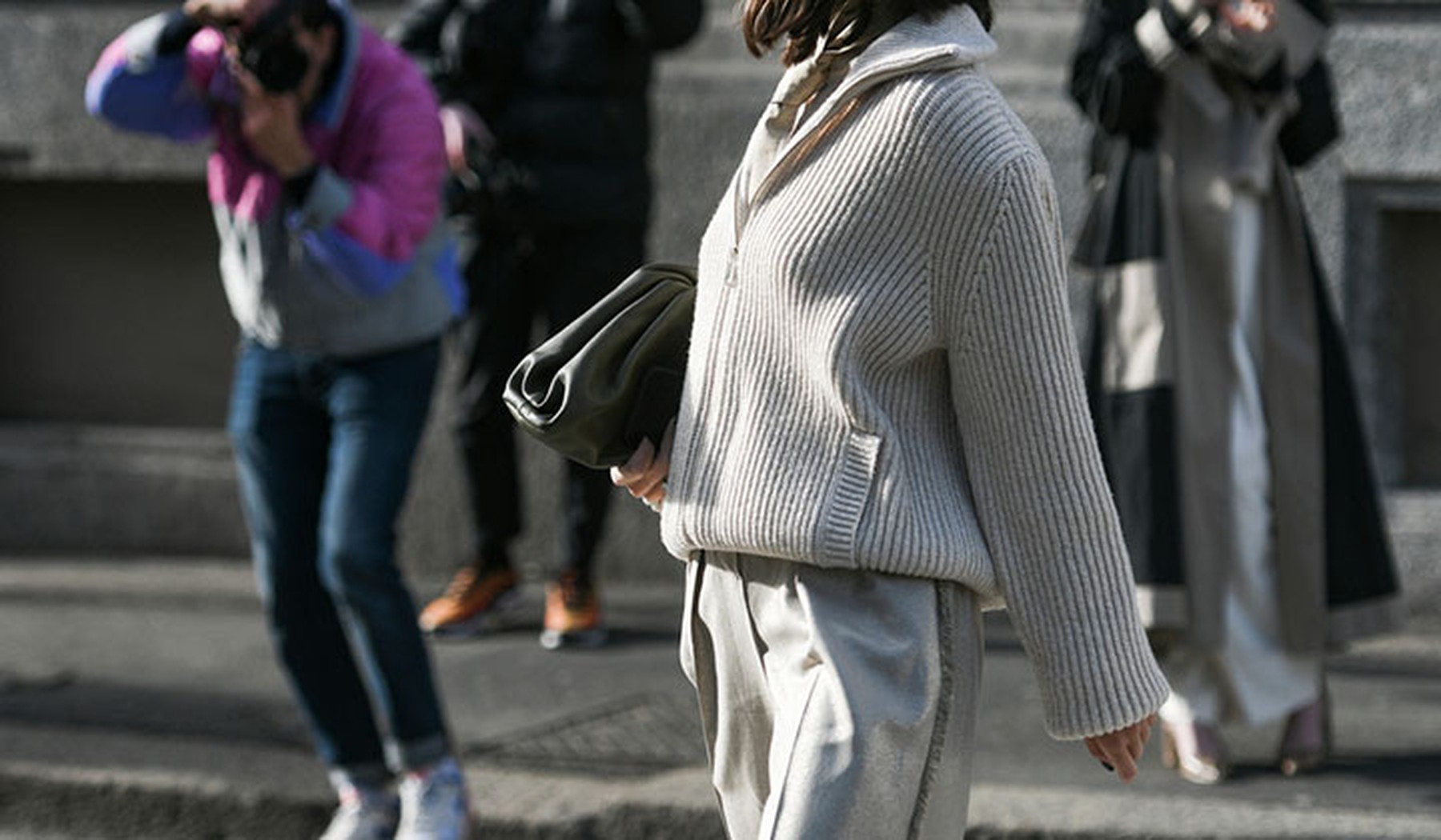 Mujer con un jersey y pantalón gris claro y un bolso en el brazo de color negro