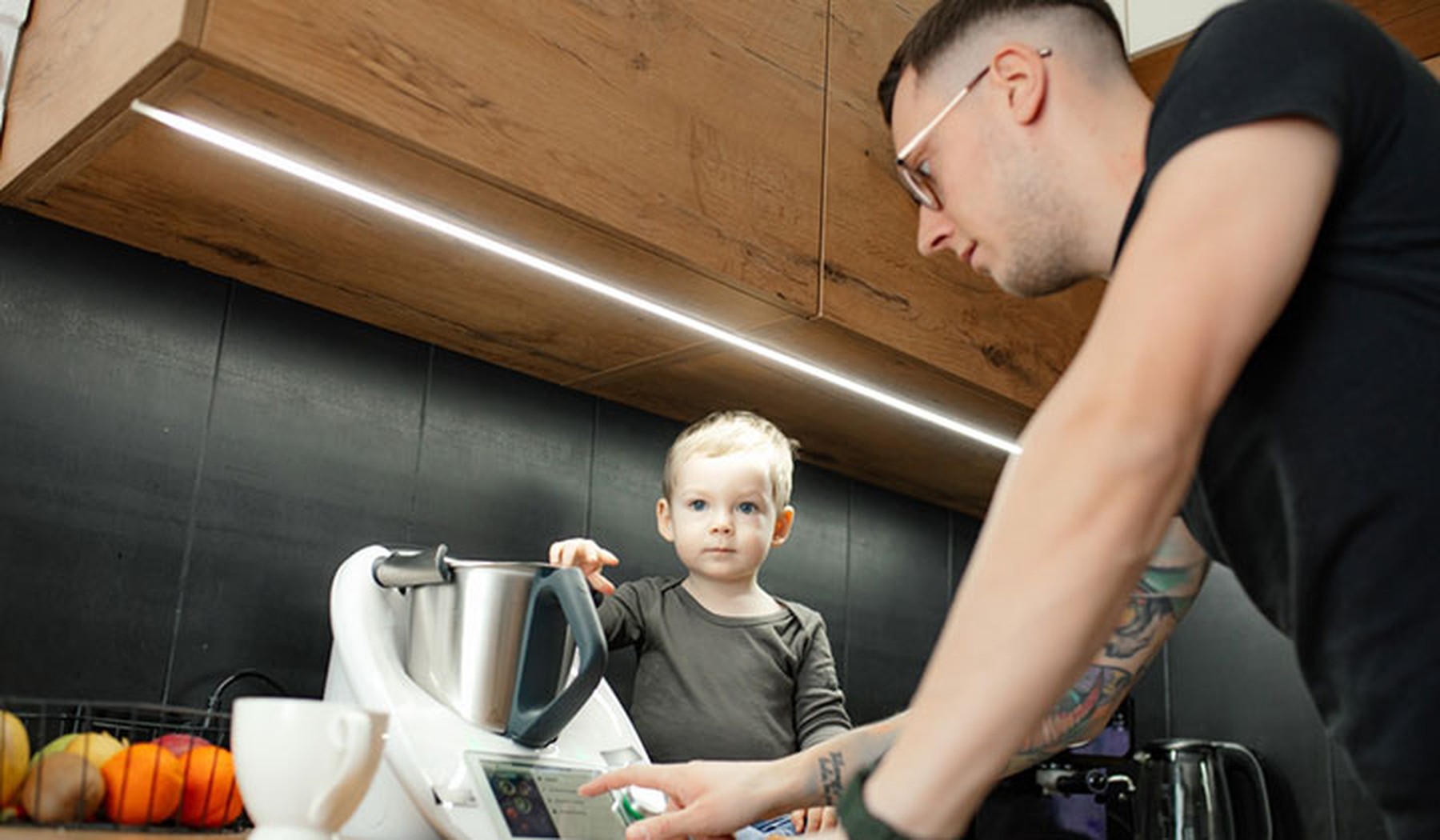 Padre joven con su bebé en la cocina utilizando un robot de cocina