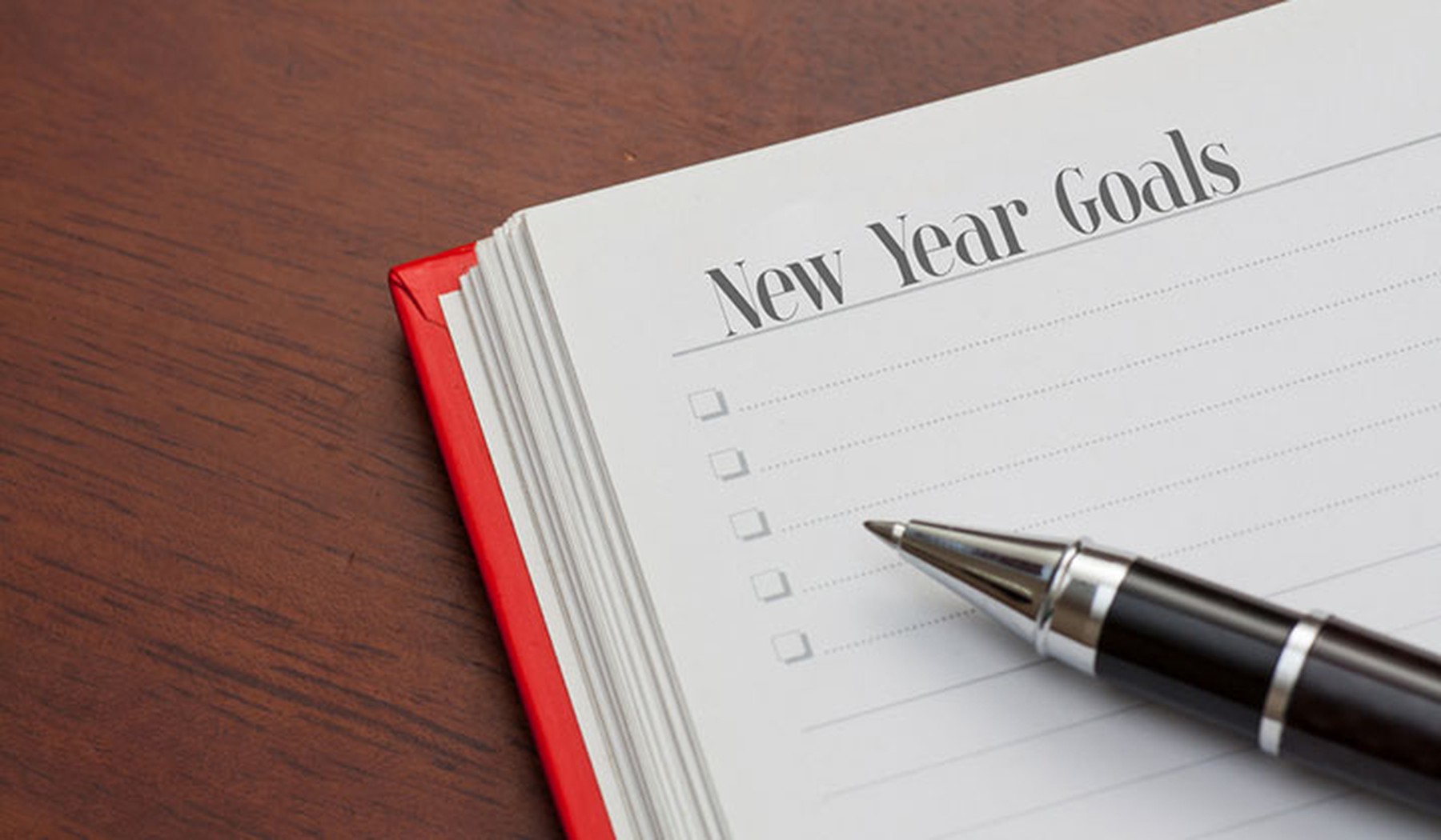 Cuaderno con New Year Goals sobre una mesa de madera y con un bolígrafo negro encima