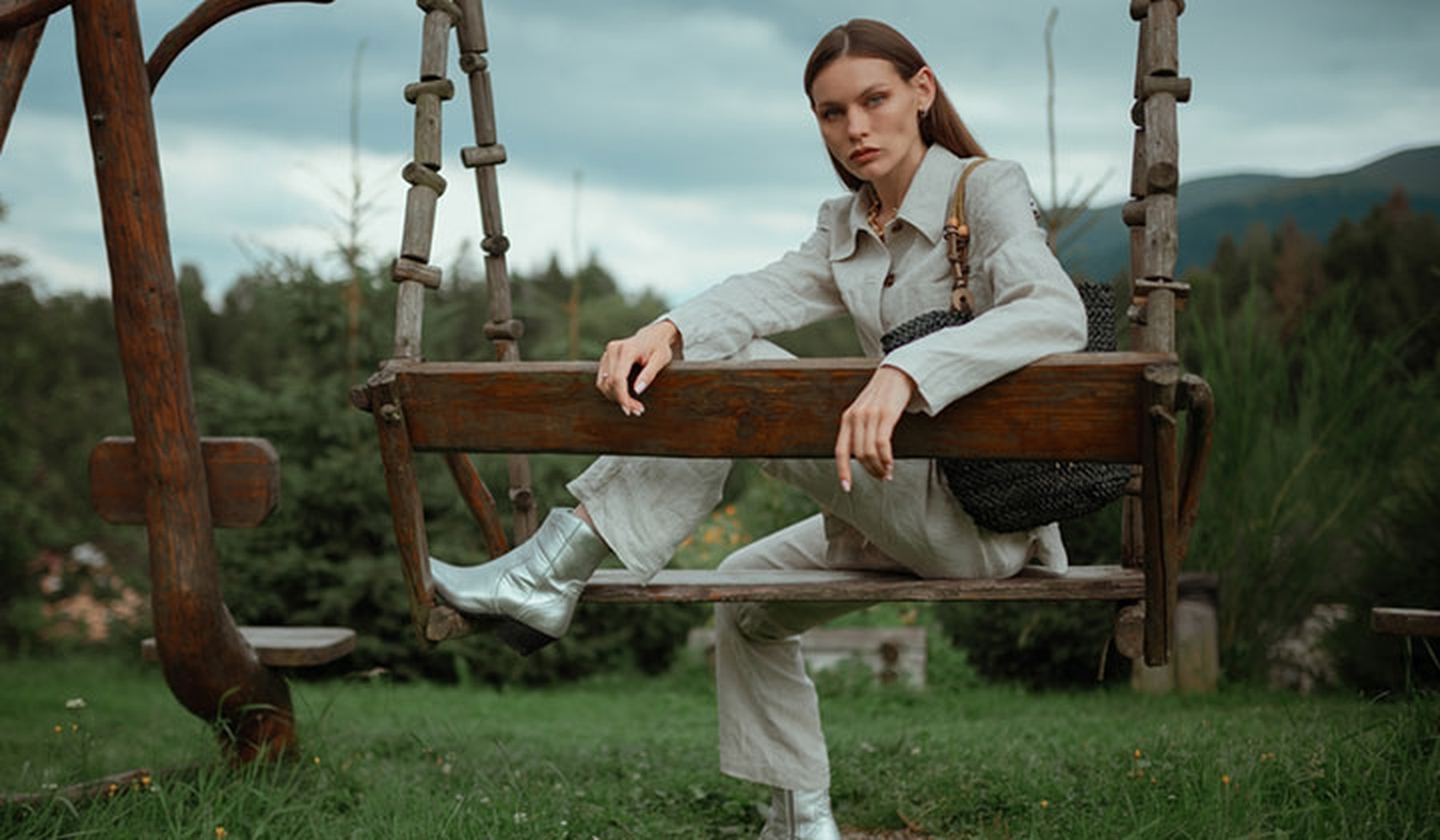 Mujer joven sentada en un columpio de madera con ropa vaquera blanca y unos botines plateados
