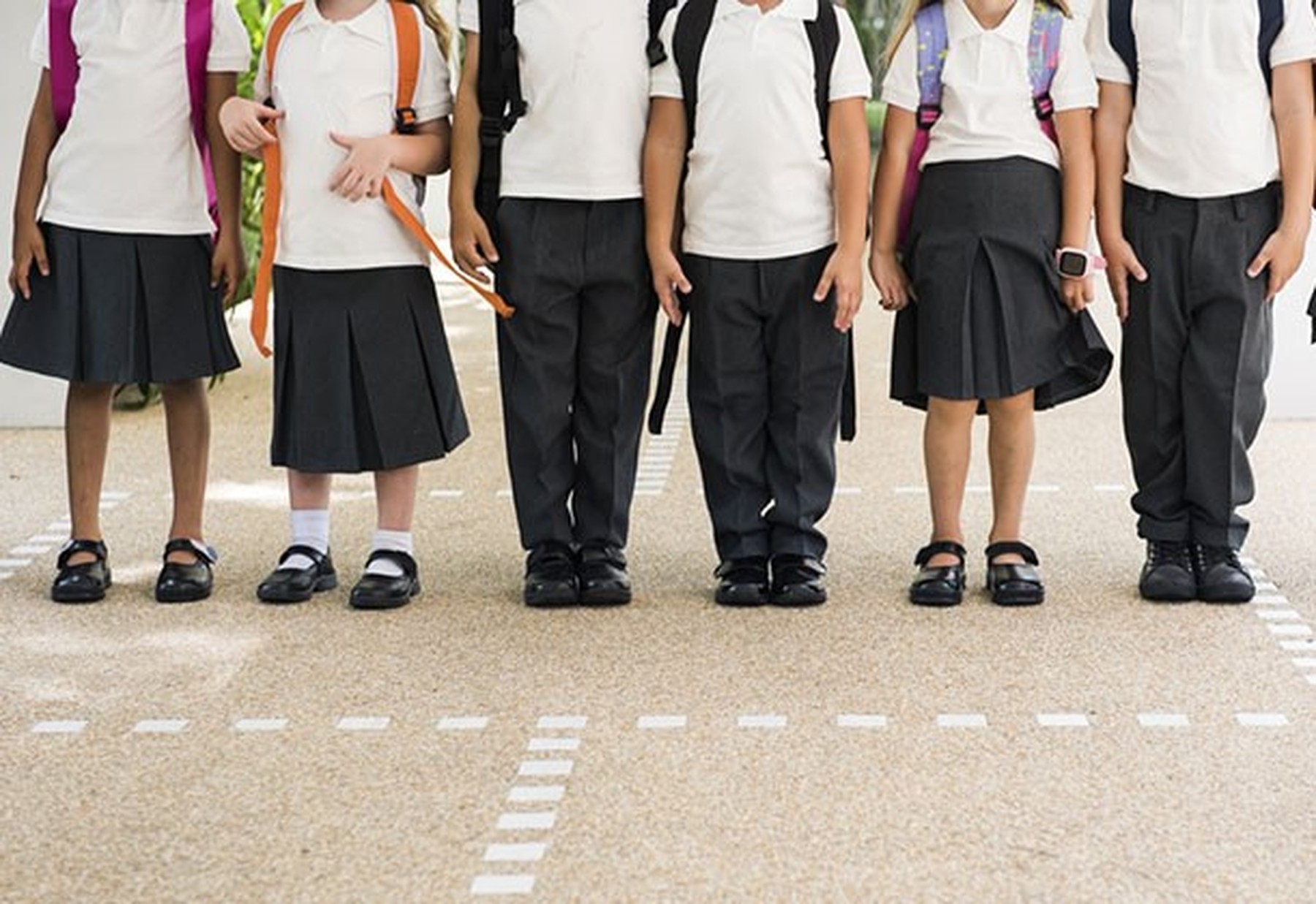 Niños y niñas en el patio de un colegio vistiendo uniforme de falda o pantalón negro y polo blanco