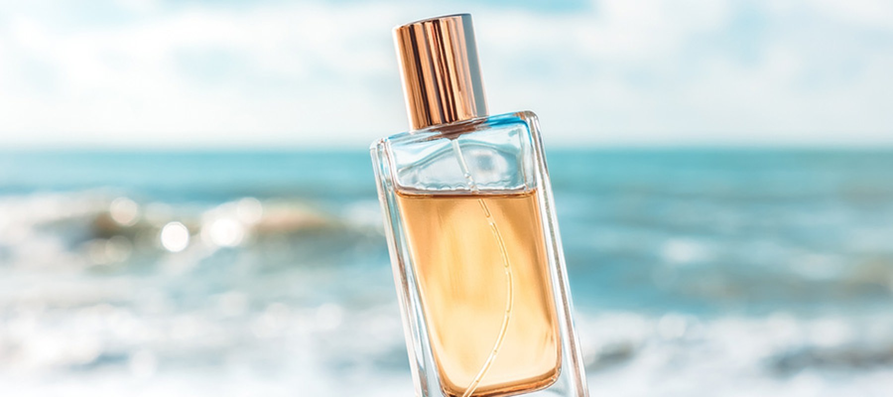 Botella de perfume dorado cerca del mar