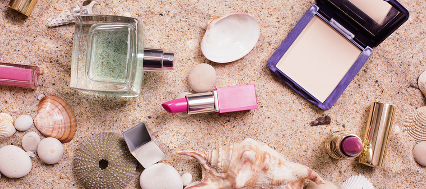 Productos de maquillaje, un perfume, conchas y caracolas sobre arena de playa
