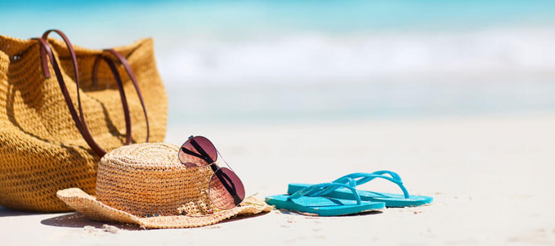 Bolsa, sombrero, gafas y chancla sobre la arena de una playa