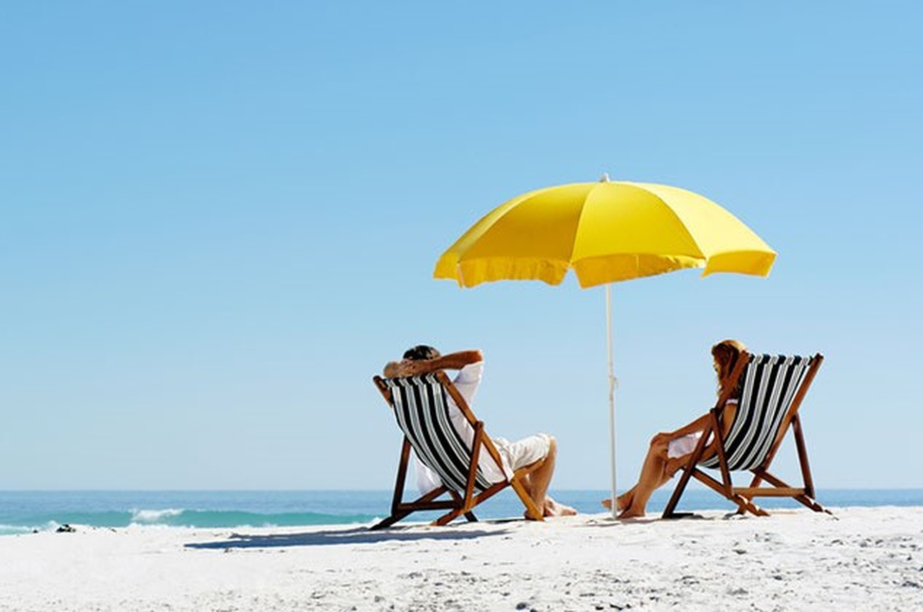 Pareja de verano en la playa durante unas vacaciones en una isla con una sombrilla amarilla