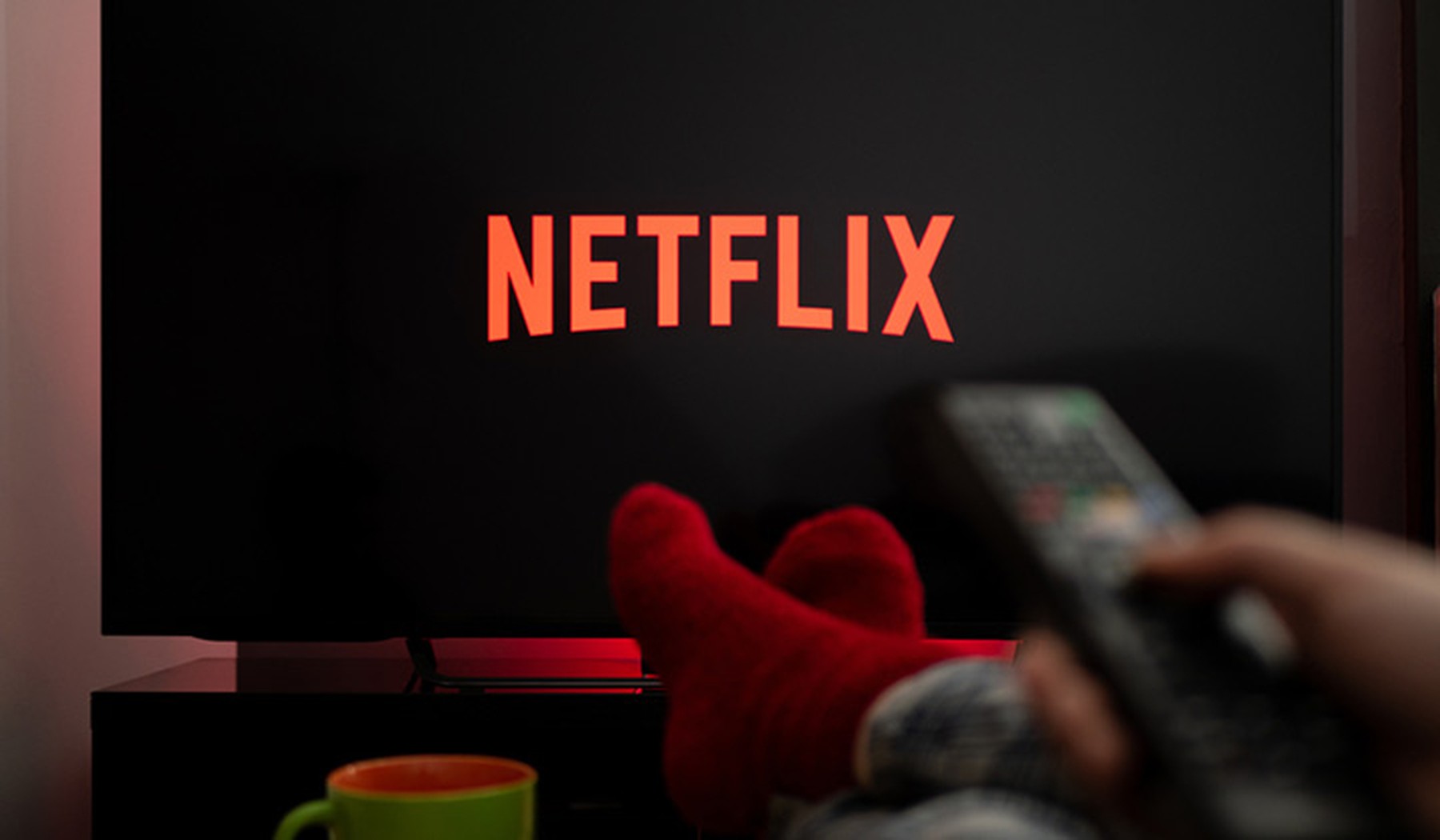 Pantalla de televisión con el logo de Netflix y una persona con calcetines rojos usando el mando de la TV