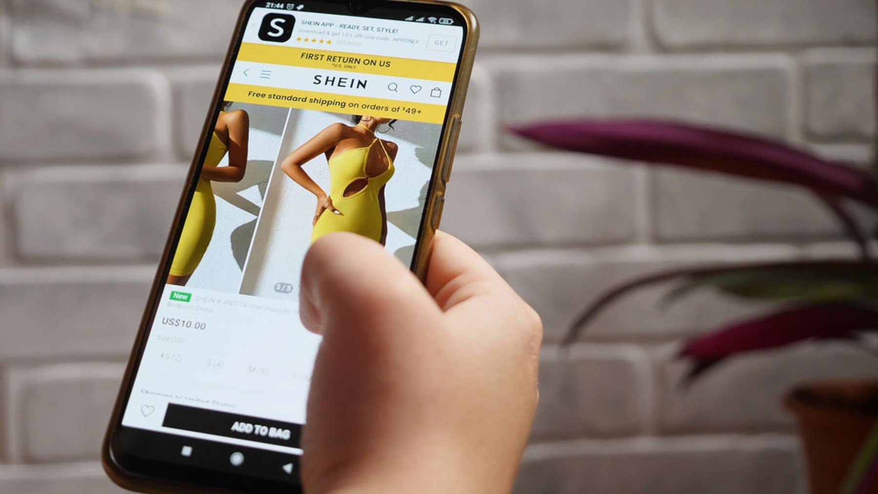 Smartphone con un vestido de SHEIN amarillo en pantalla y una mano utilizándolo