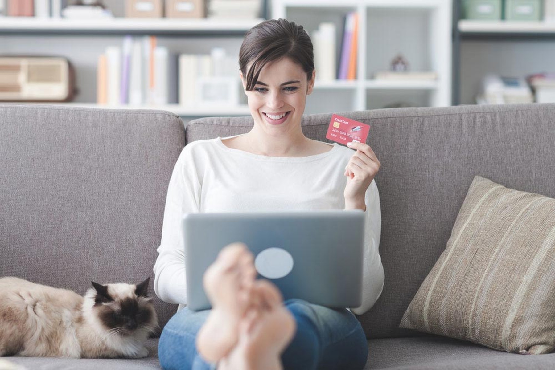 Mujer sonriente sentada en el sofá con su gato mientras hace una compra online en su portátil