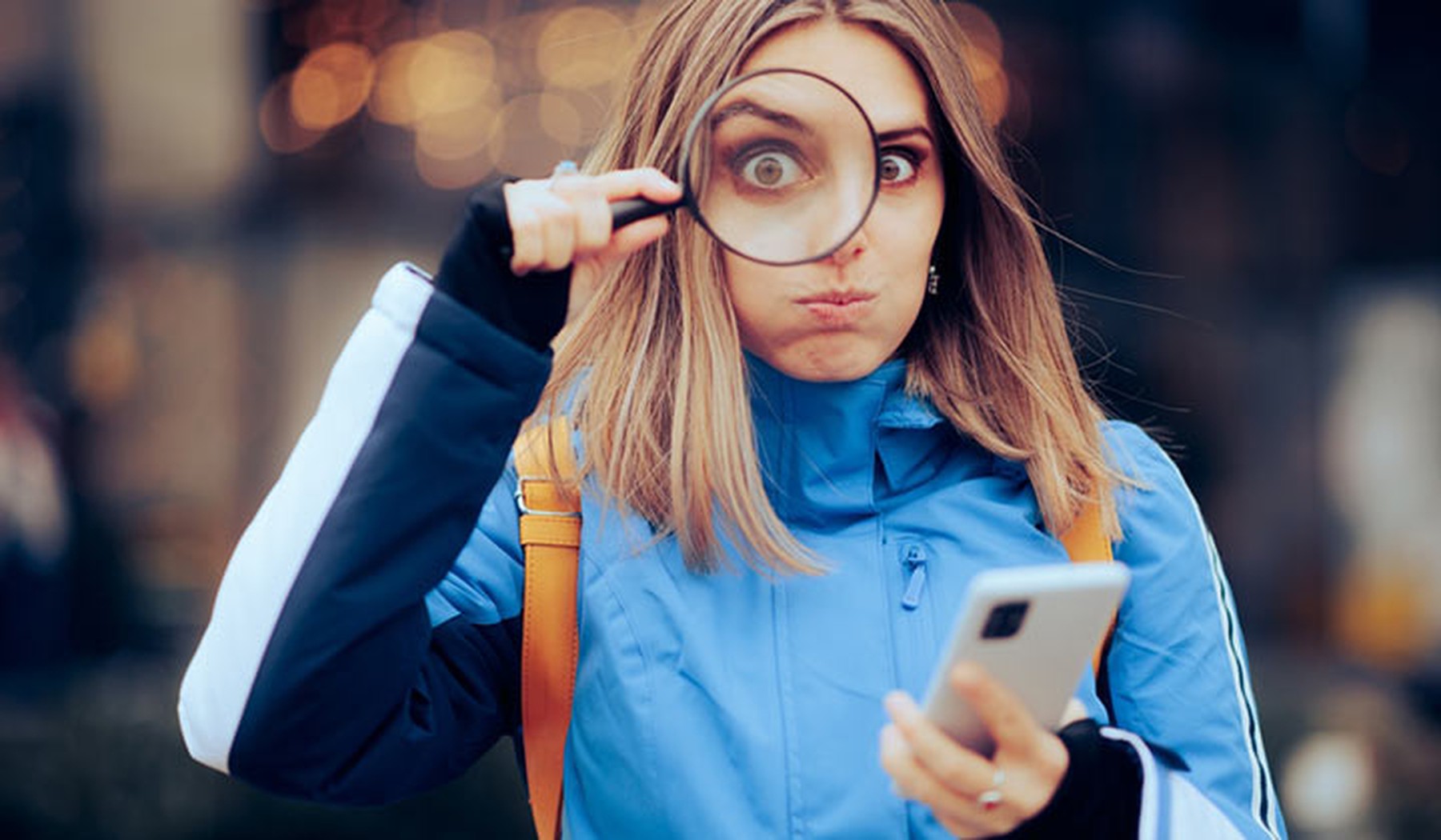 Divertida mujer buscando en Internet en su teléfono móvil con una lupa sobre un ojo.