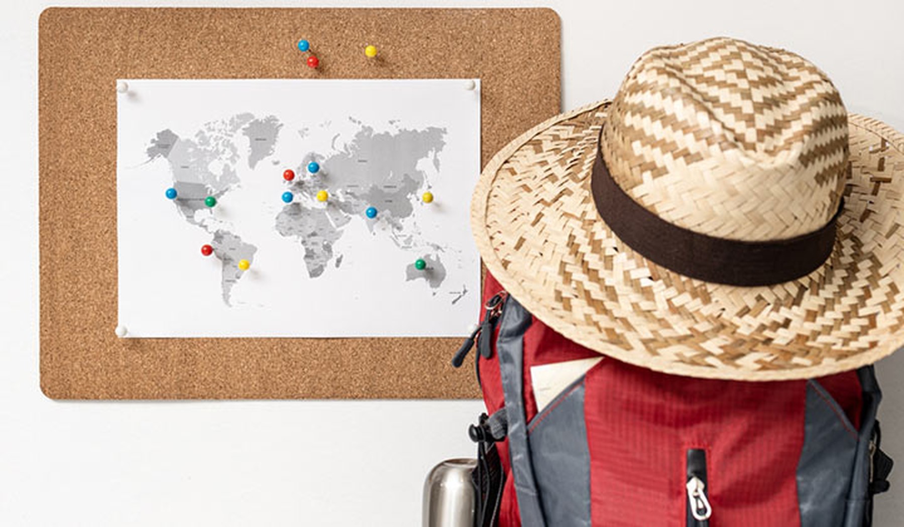 Corcho con mapa del mundo y pines en la pared, mochila y sombrero de verano