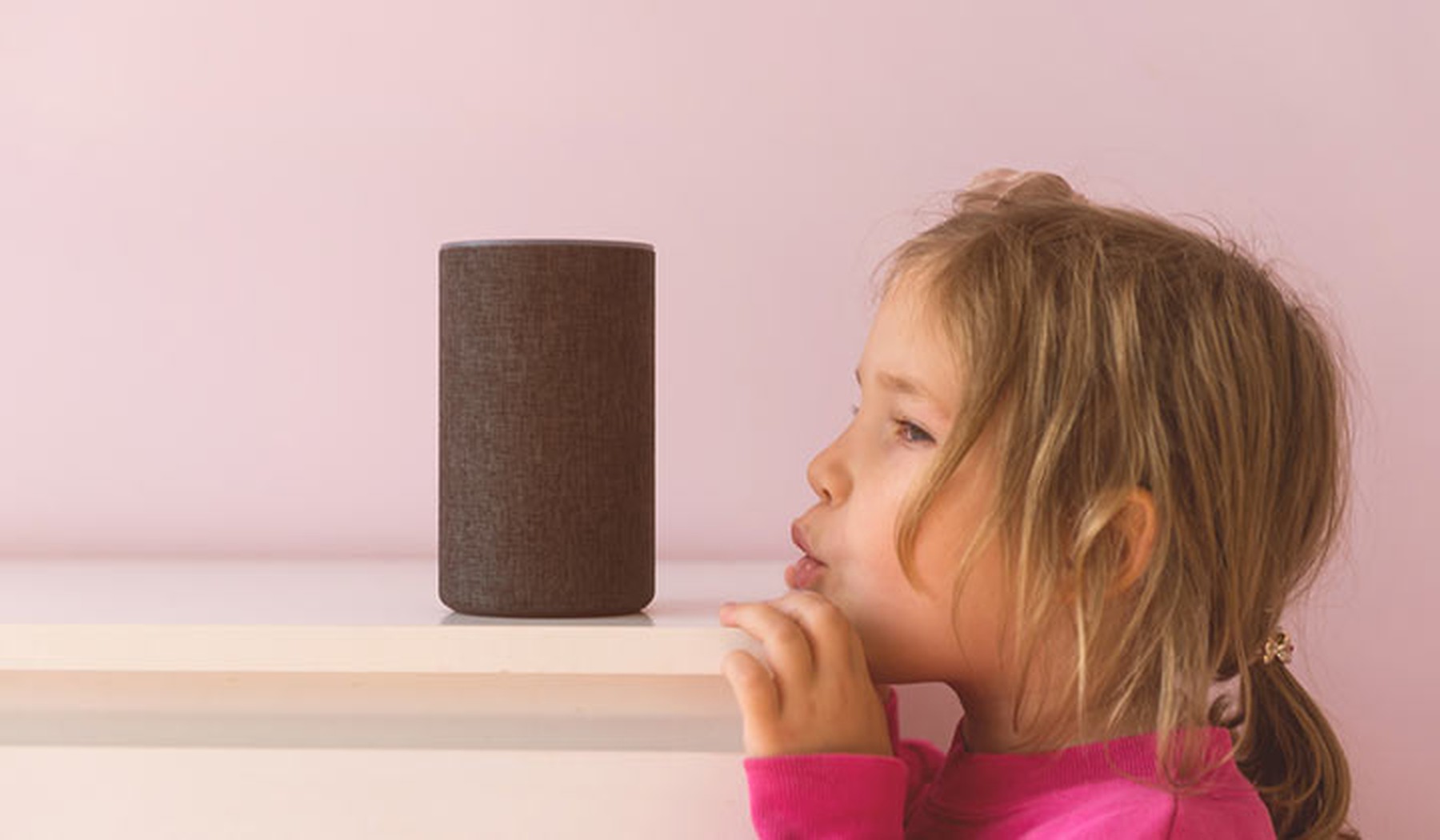 Niña pequeña vestida de rosa hablando con Amazon Alexa Echo Dot.