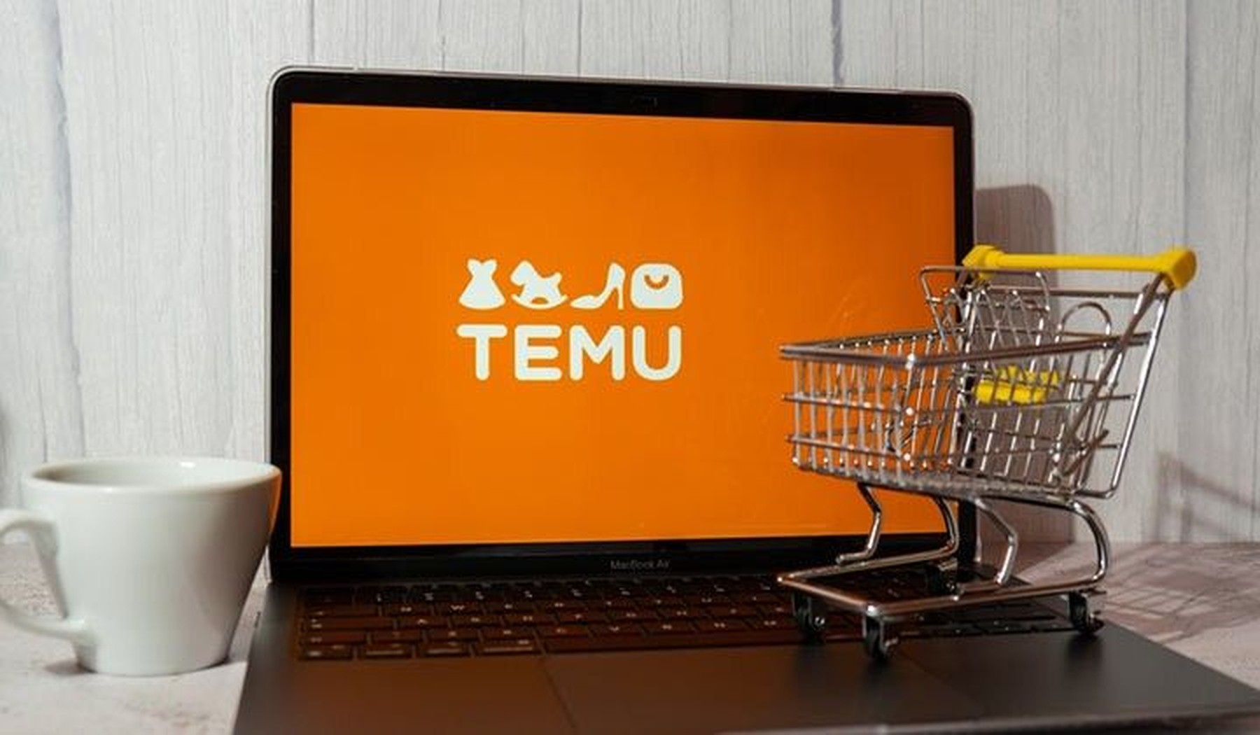 Ordenador con la página de Temu en la pantalla y un carrito de compra pequeño al lado 