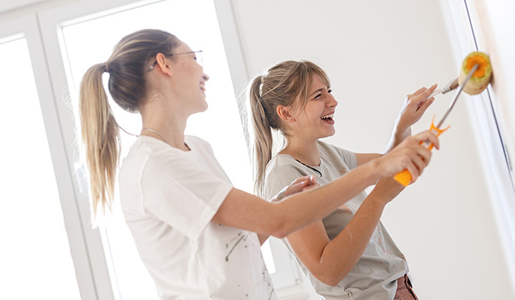 Dos mujeres jóvenes usan un rodillo de pintura para decorar las paredes de su nuevo hogar.