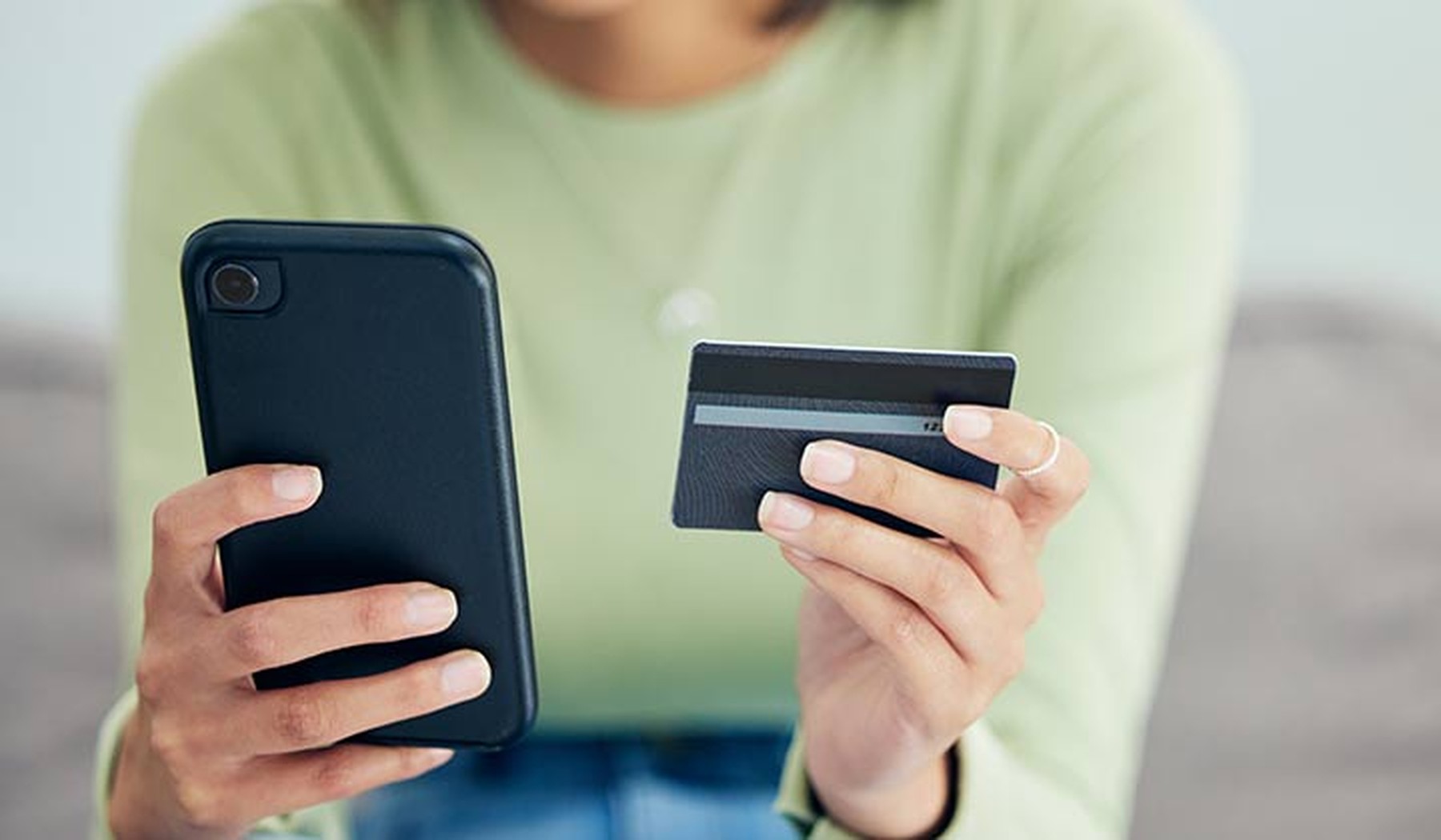 Mujer en un sofá con una tarjeta de crédito en una mano y su smartphone en otra