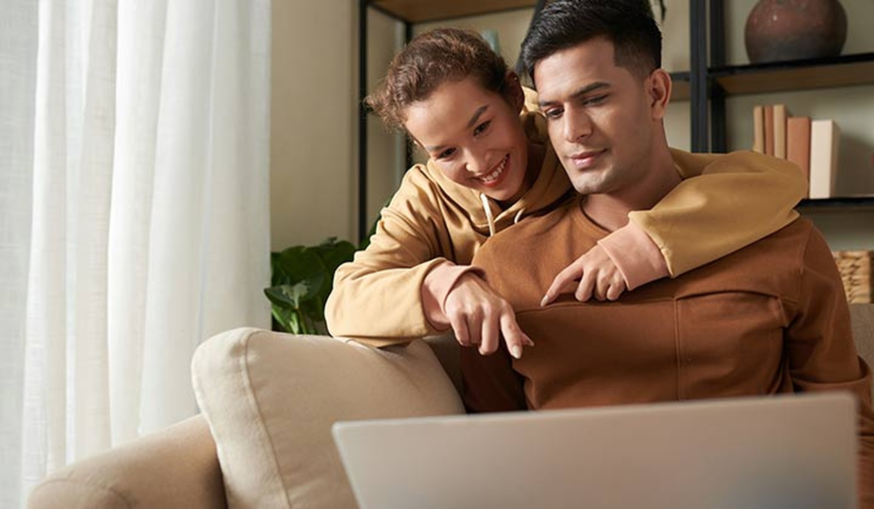 Mujer joven apuntando con el dedo a la pantalla de un portátil y eligiendo artículos para comprar online junto a su pareja