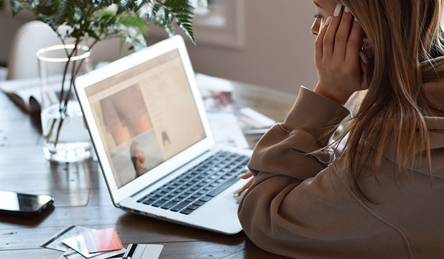 Mujer joven sentada en la mesa con ordenador portátil para comprar ropa en línea