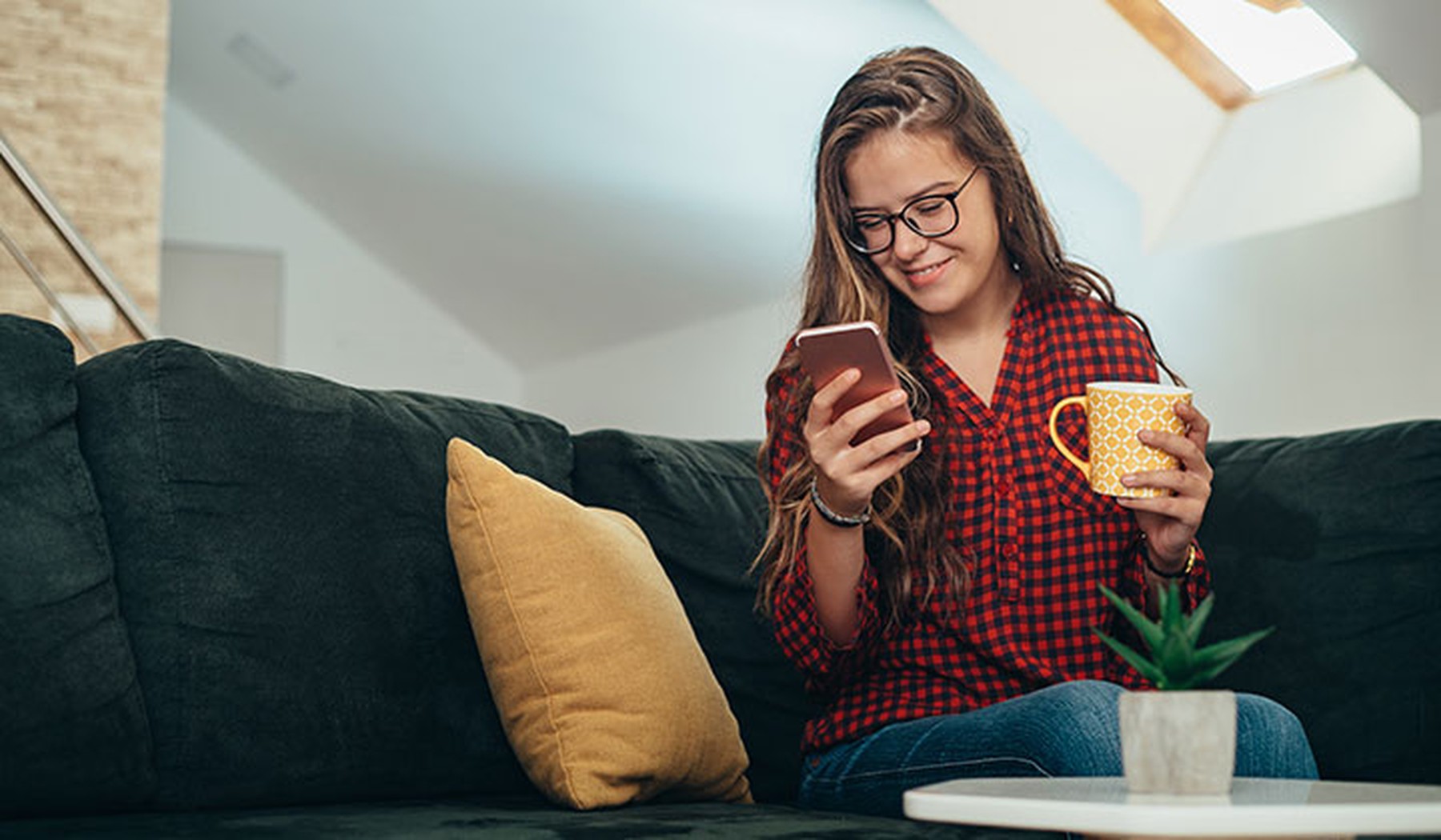 Plano completo de una joven sentada en un sofá y sintiéndose emocionada mientras compra online con su smartphone.