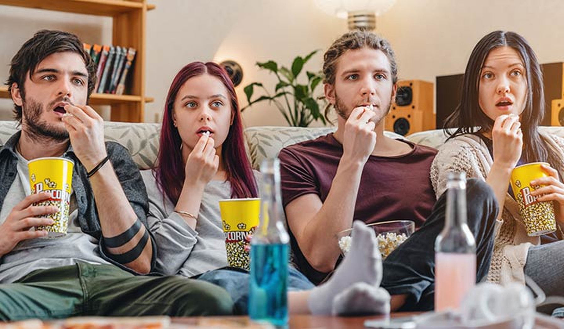 Grupo de 4 amigos sentados en un sofá y asombrados viendo una película mientras comen palomitas