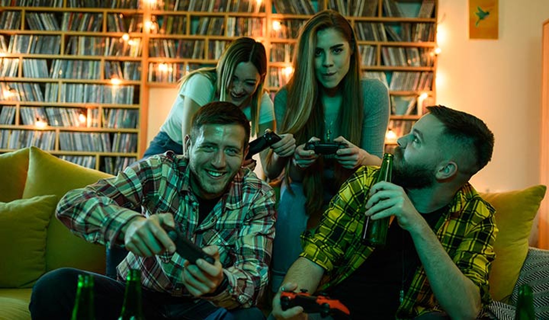 Grupo de amigos sentados en un sofá jugando a videojuegos mientras toman unas cervezas