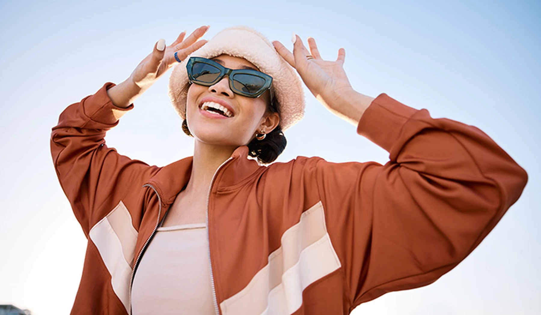 Mujer joven sonriendo con un sombrero beige y unas gafas de sol rectangulares