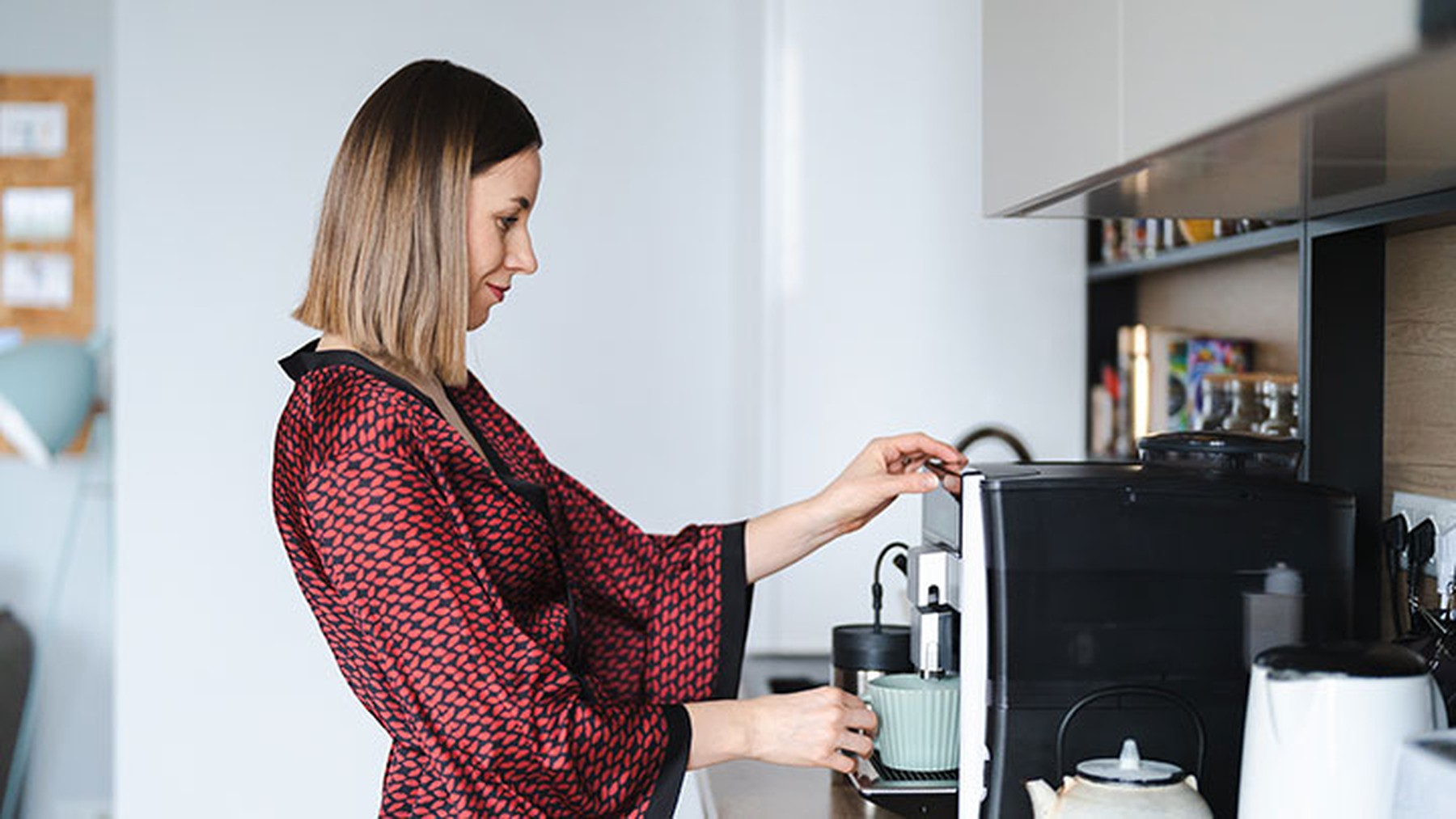 Mujer joven con una bata preparando café en una cafetera automática en su casa por la mañana.