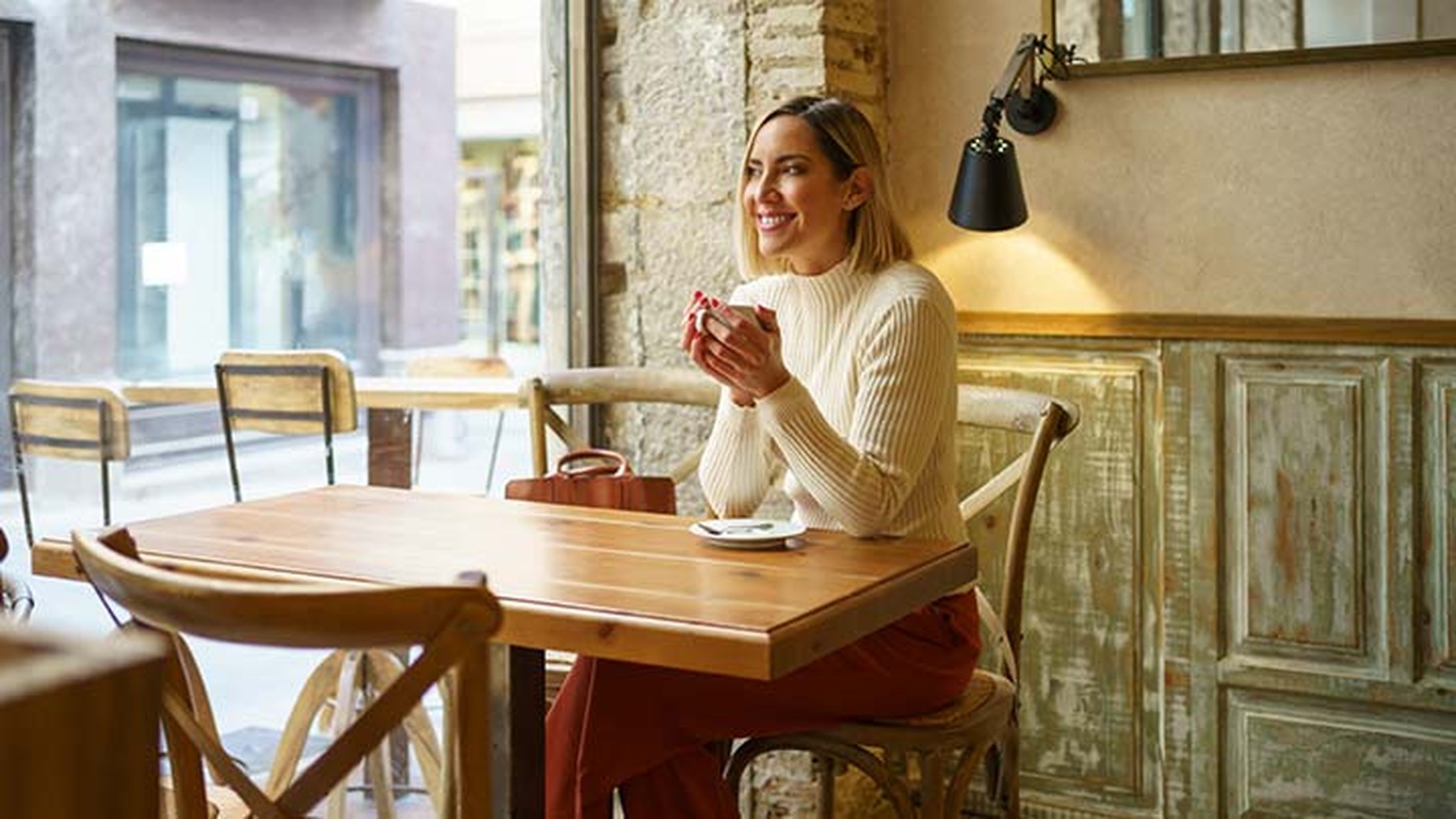 Mujer sonriente sentada en una cafetería con una taza de café en sus manos.