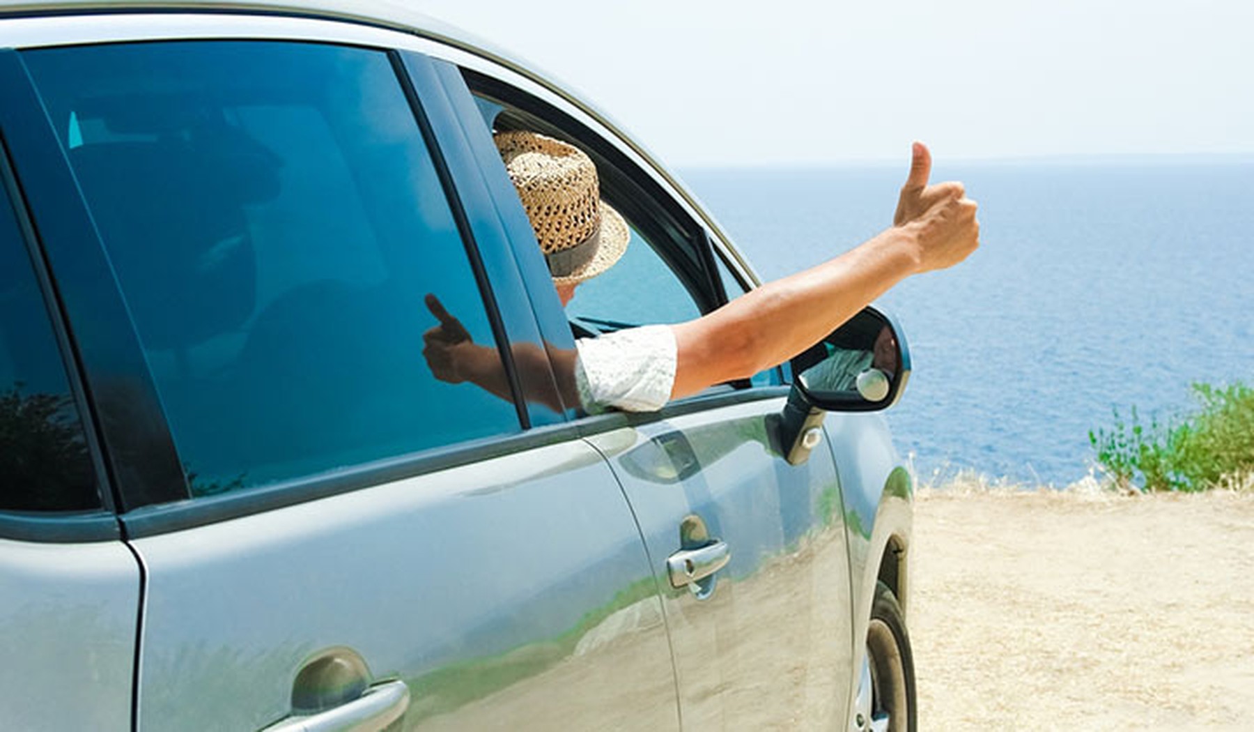 Persona sacando la mano por la ventanilla de un coche frente a la playa