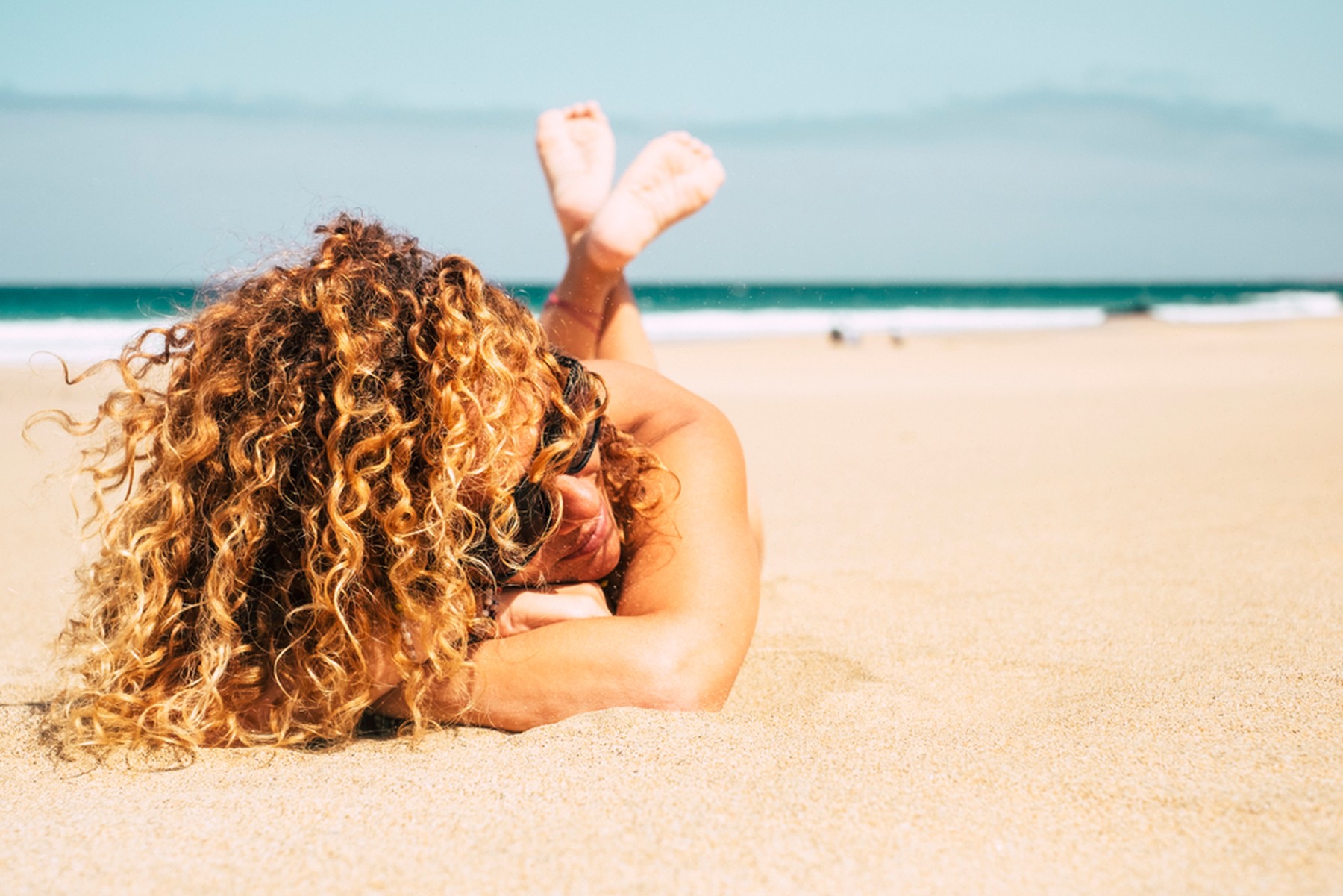 Mujer rubia con el pelo rizado tumbada en la playa al sol