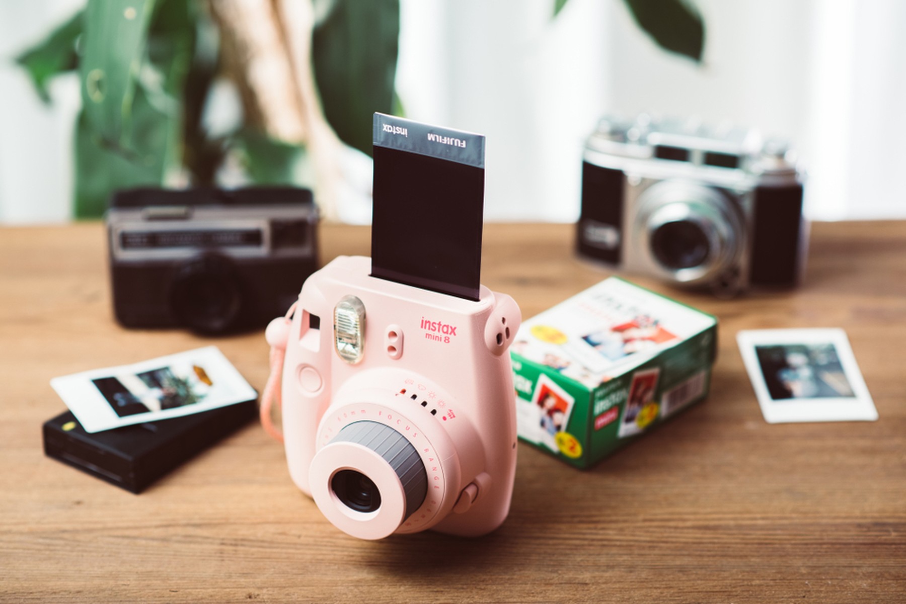 Cámara Fujifilm Instax mini 8 rosa sobre una mesa de madera. Detrás hay otras cámaras.